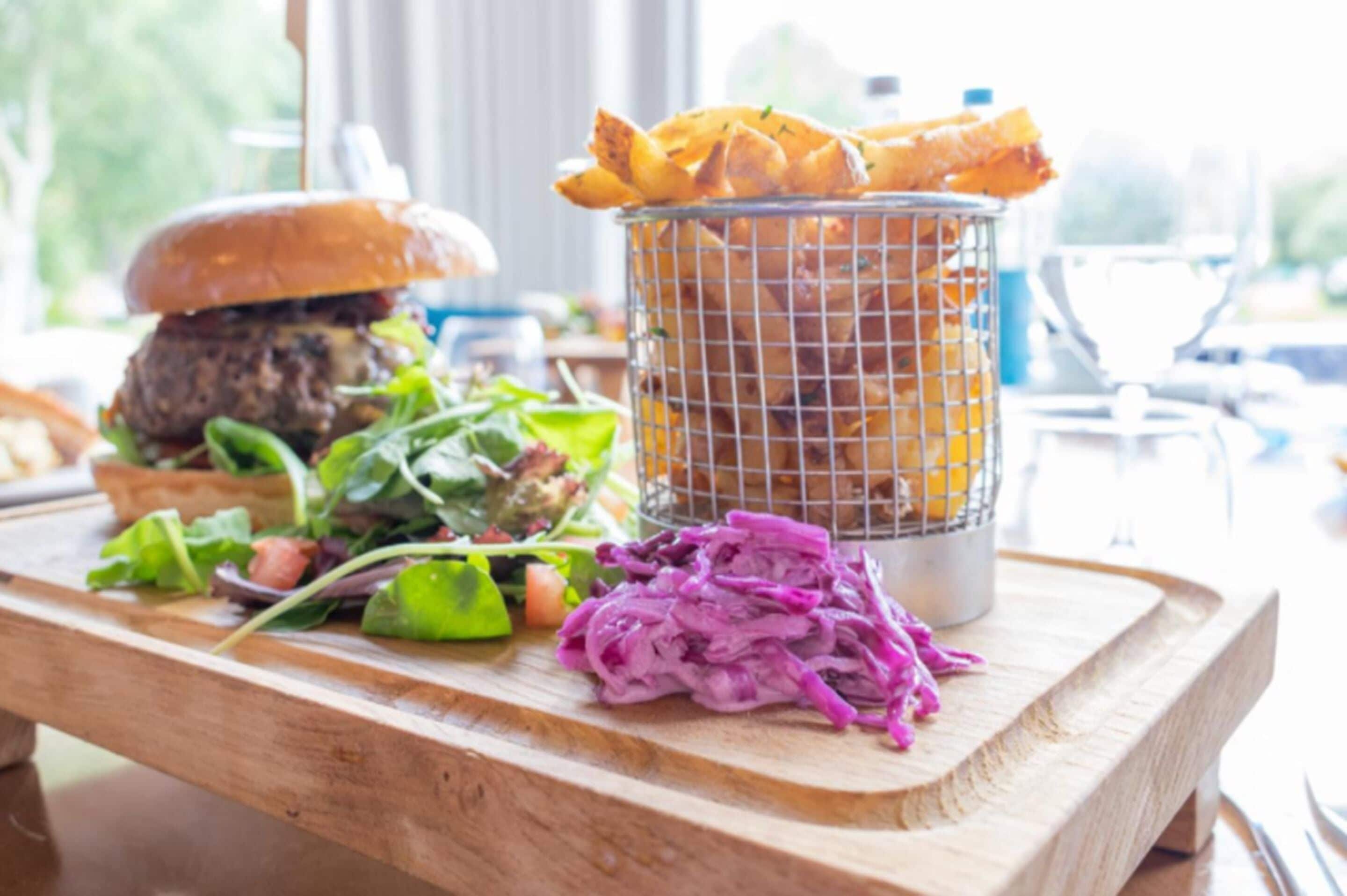 A wooden table with a burger, a basket of fries, a salad, and a pile of purple cabbage.