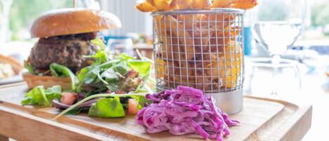 A wooden table with a burger, a basket of fries, a salad, and a pile of purple cabbage.