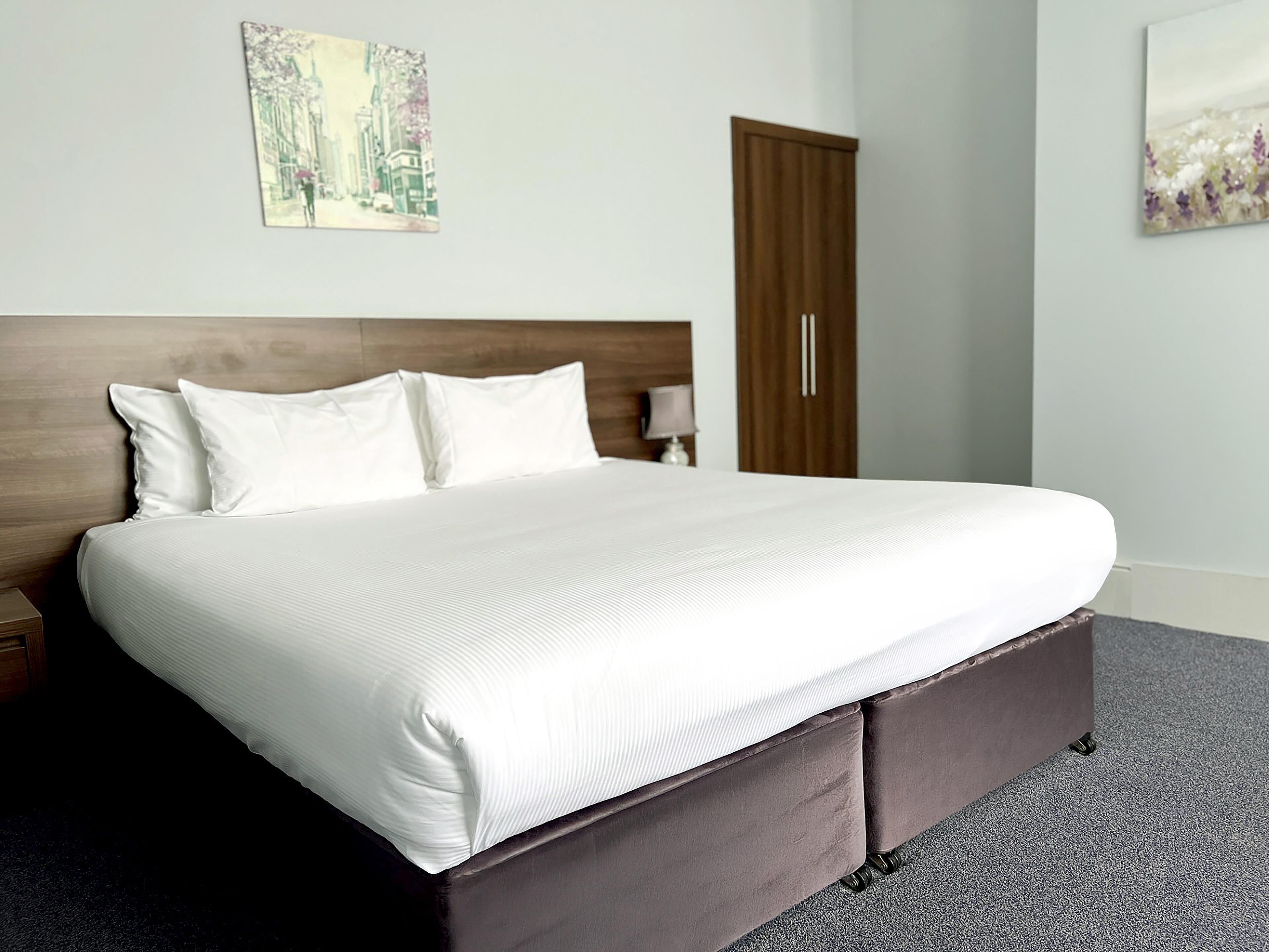 Una cama bien hecha con ropa blanca, un cabecero de madera y un piecero de color marrón oscuro.