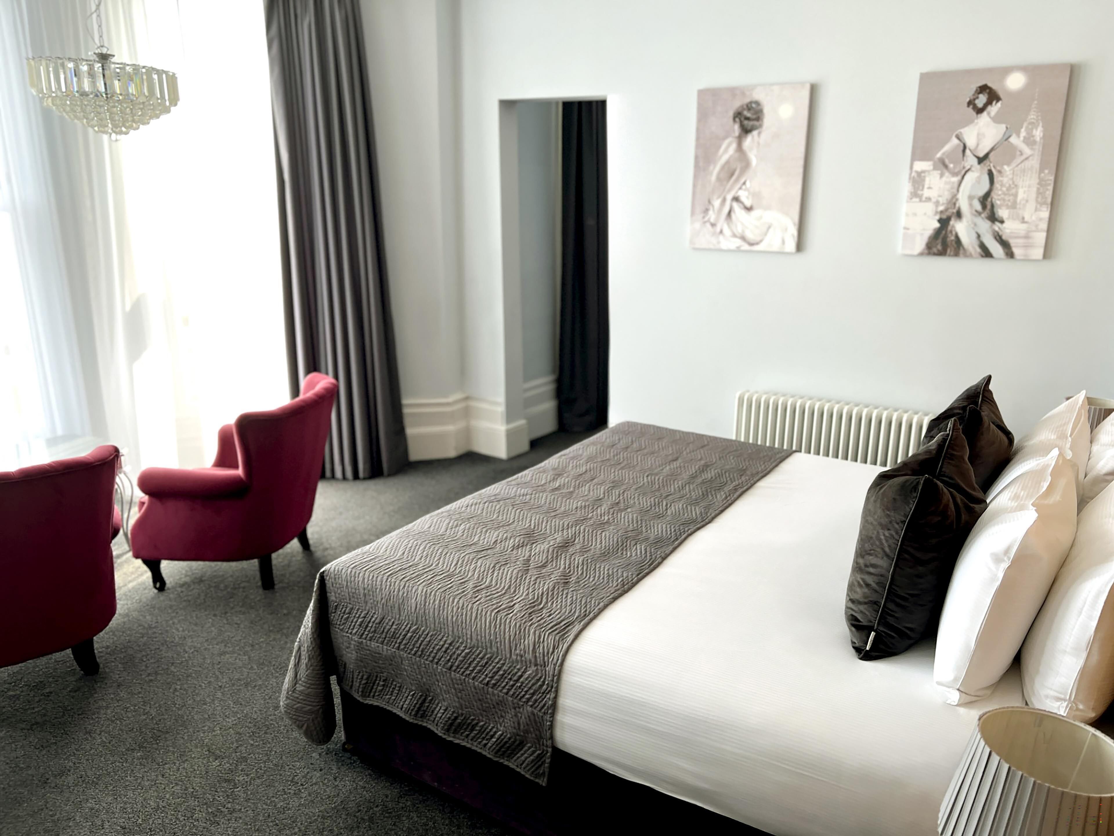 Une chambre d’hôtel avec un grand lit, un fauteuil rouge et deux œuvres d’art accrochées au mur.