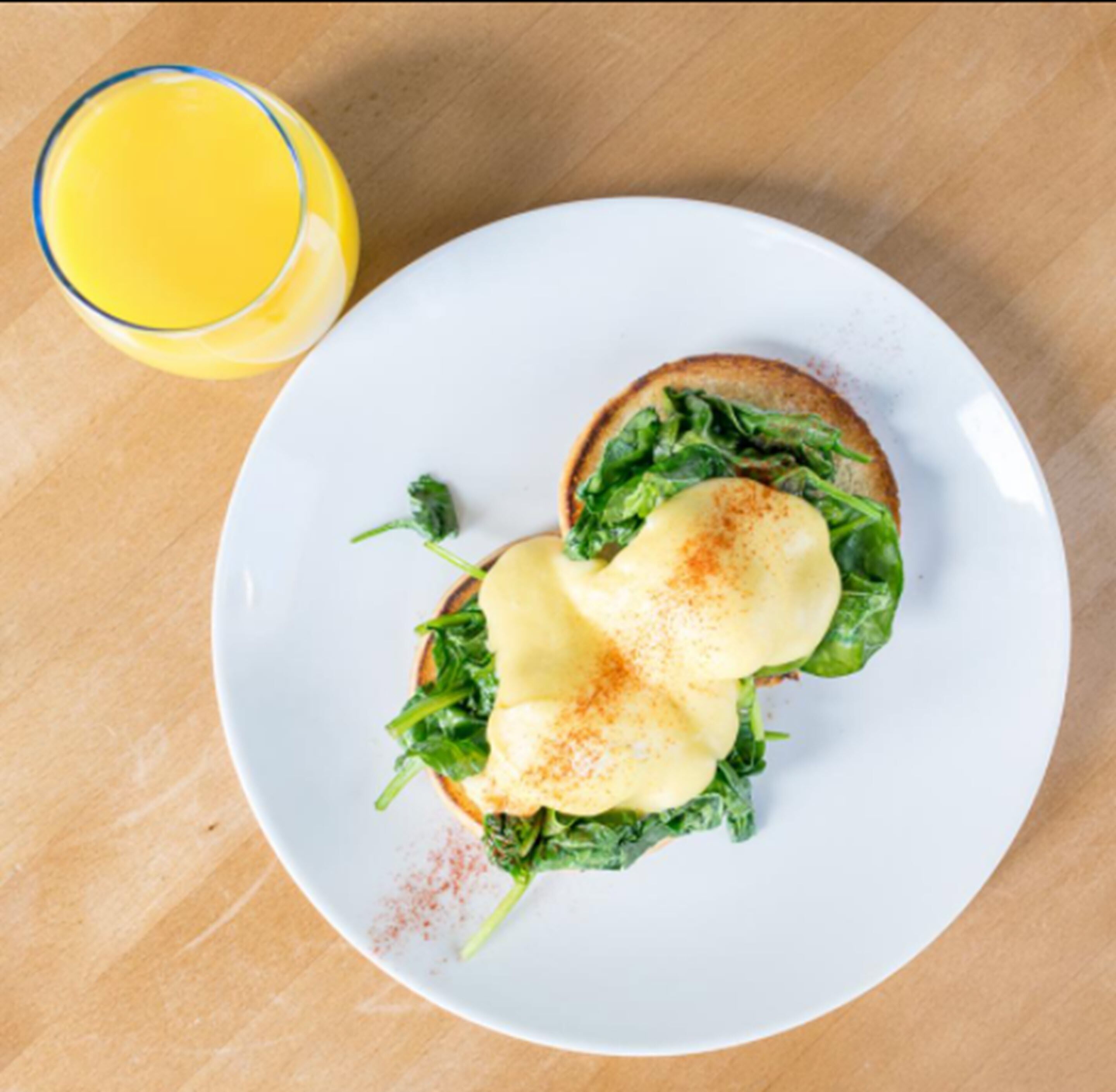 A plate with a sandwich and a glass of orange juice on a wooden table.
