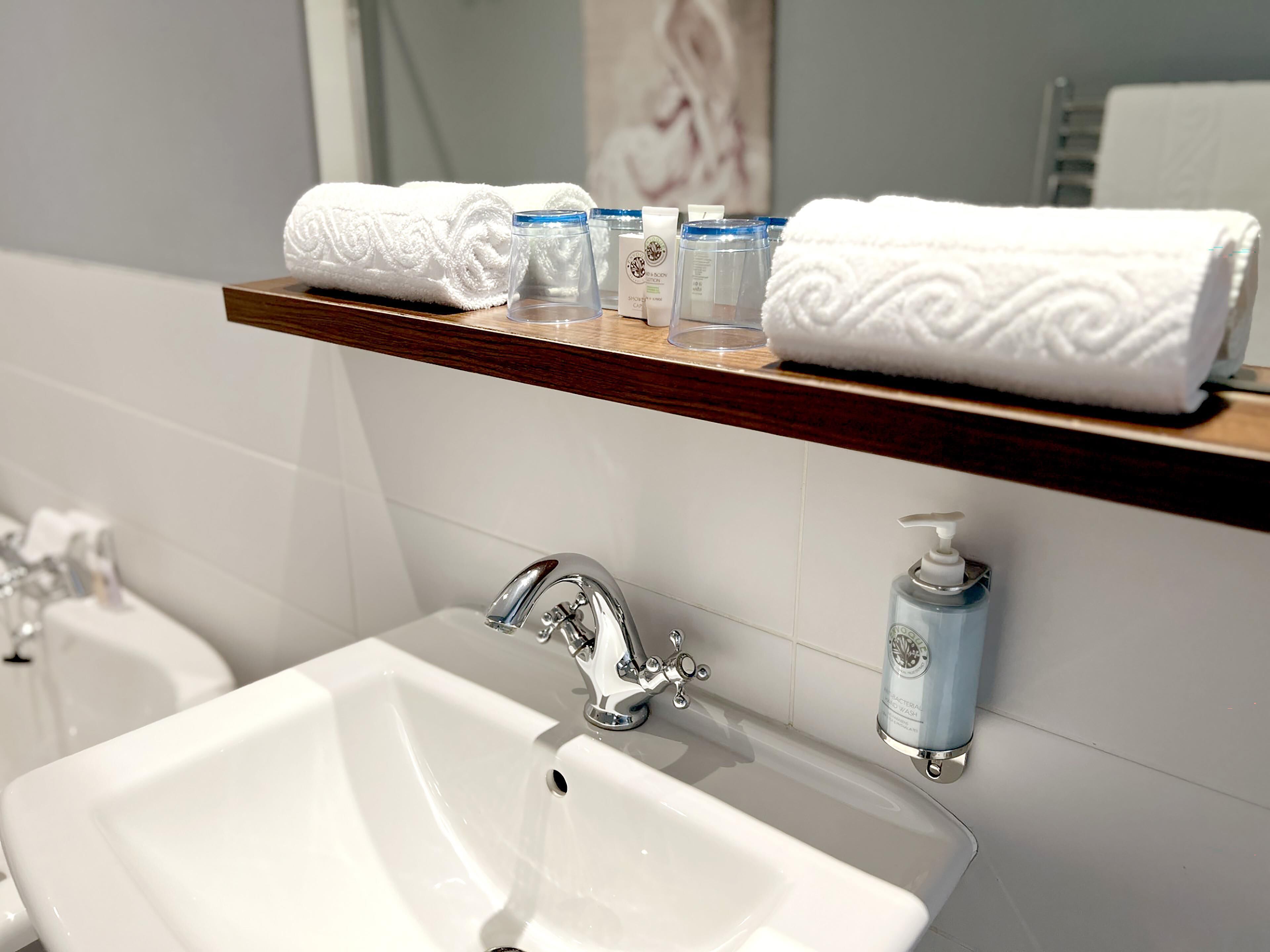 A bathroom with a white sink, a mirror, and a shelf with towels and toiletries.