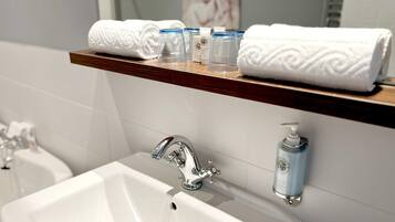A bathroom with a white sink, a mirror, and a shelf with towels and toiletries.