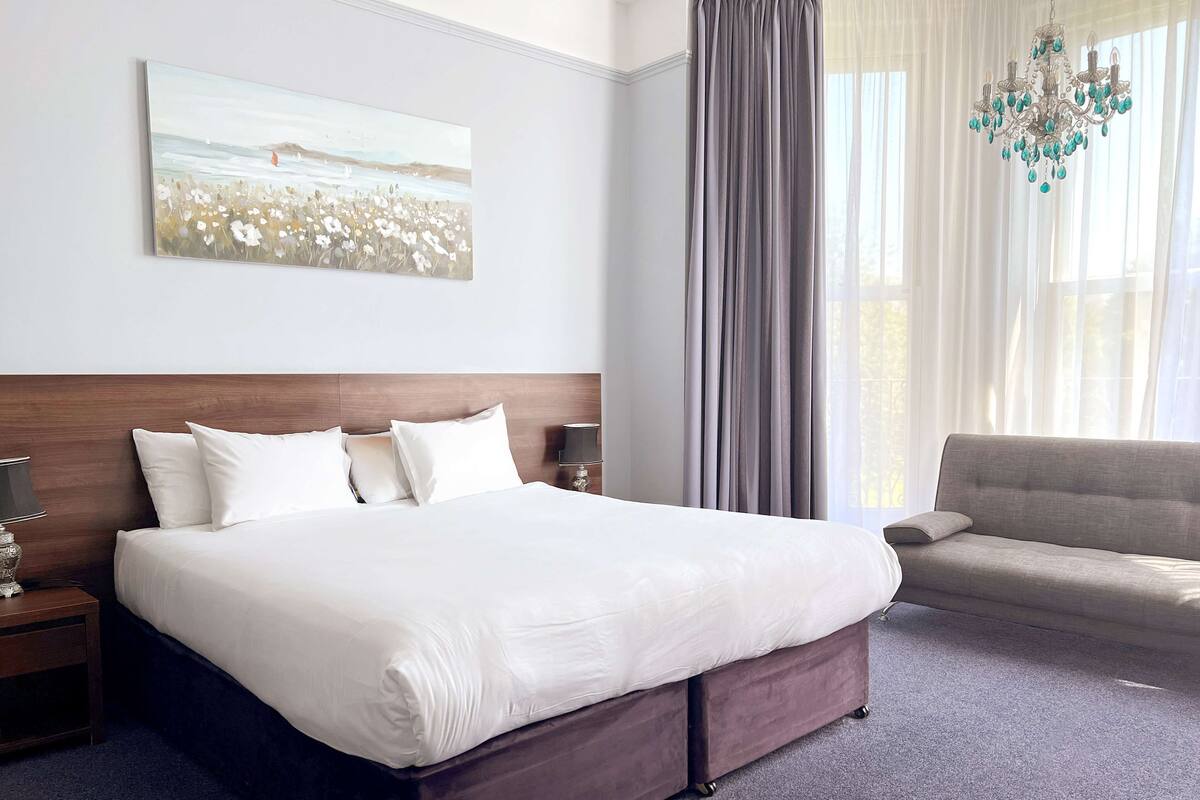Quarto de hotel com uma cama grande, um sofá, um candelabro e um quadro na parede.