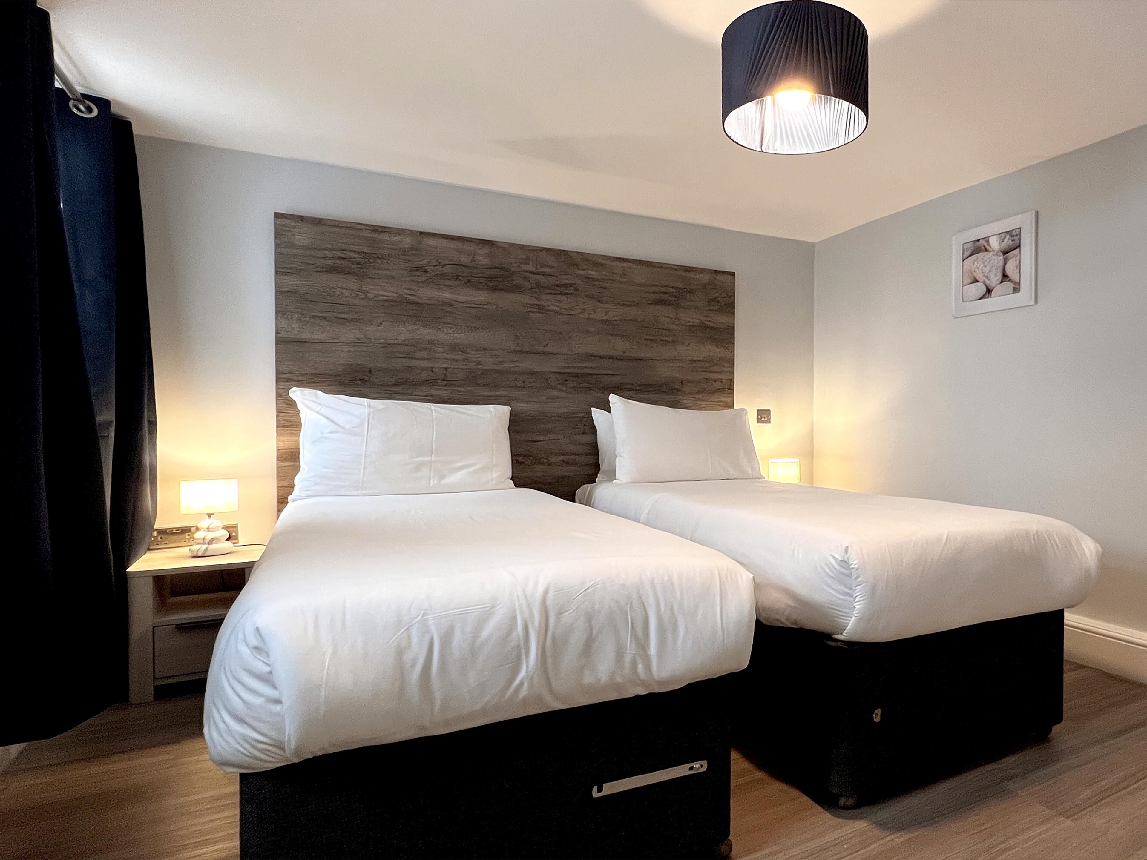 Habitación de hotel con dos camas, cabecero de madera, lámparas de noche y un cuadro en la pared.