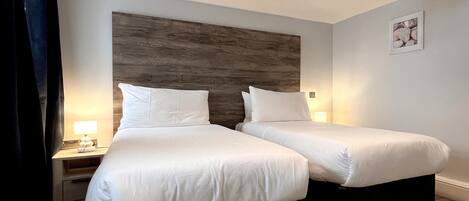 A hotel room with two beds, wooden headboard, bedside lamps, and a framed picture on the wall.