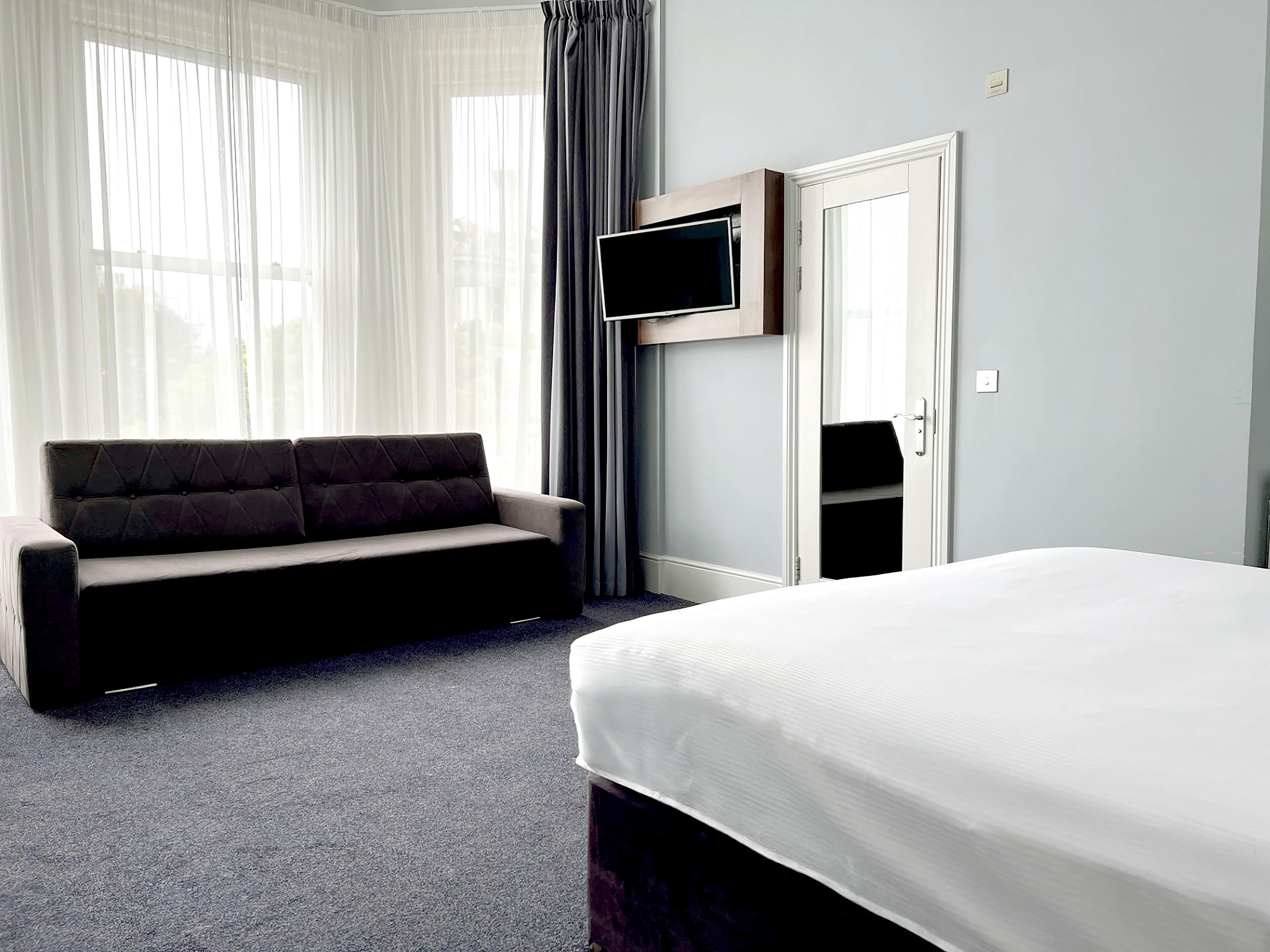 A hotel room with a bed, a sofa, a TV mounted on the wall, and a door.