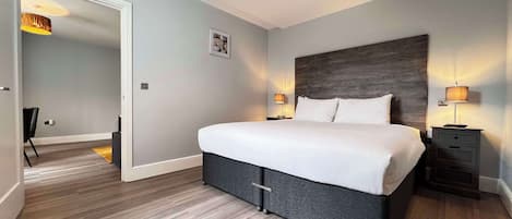 Une chambre d’hôtel moderne avec un grand lit, deux tables de chevet avec des lampes, une tête de lit en bois et un petit tableau accroché au mur.