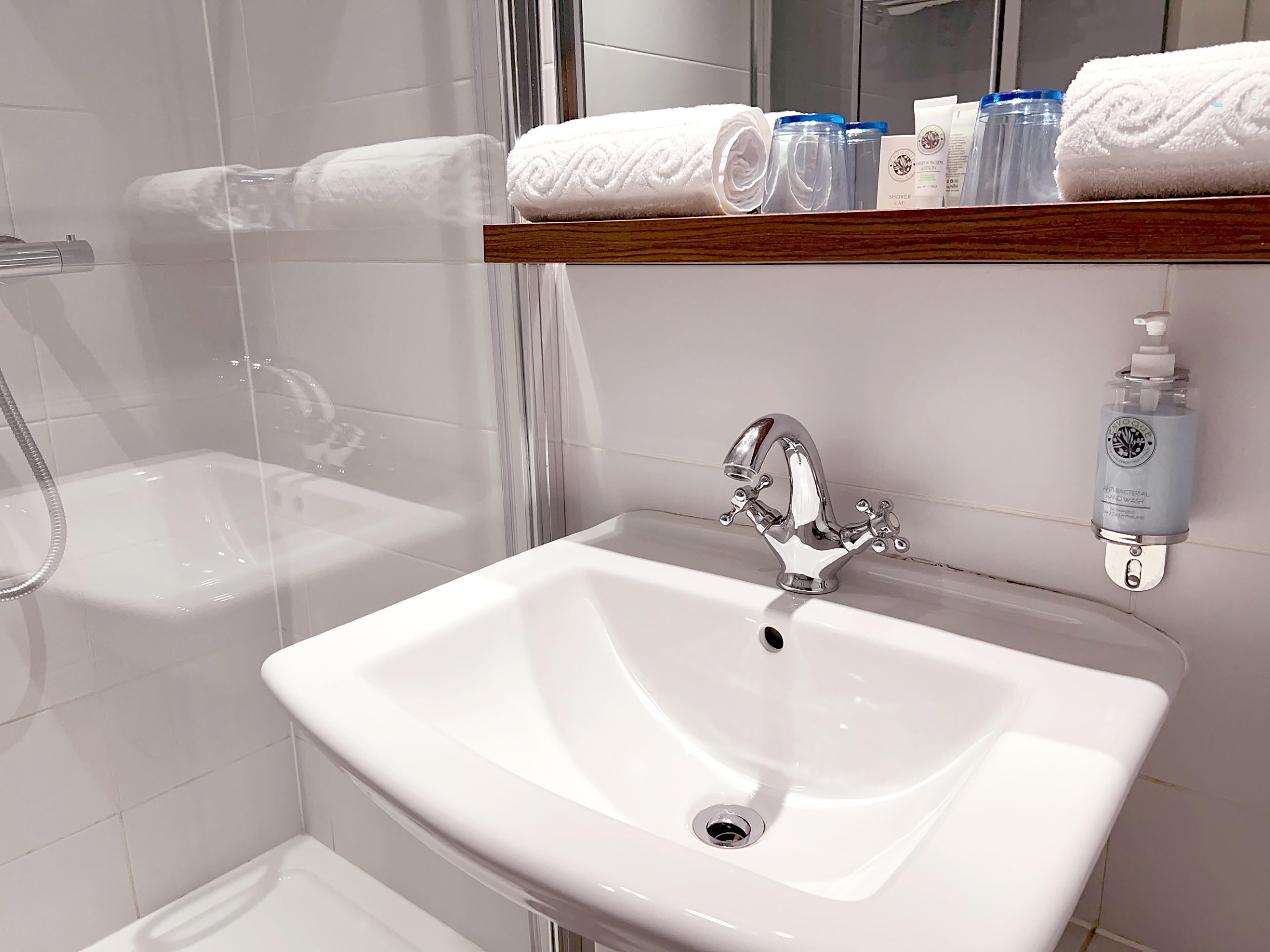 A bathroom with a white sink, a shower, and a shelf with toiletries.