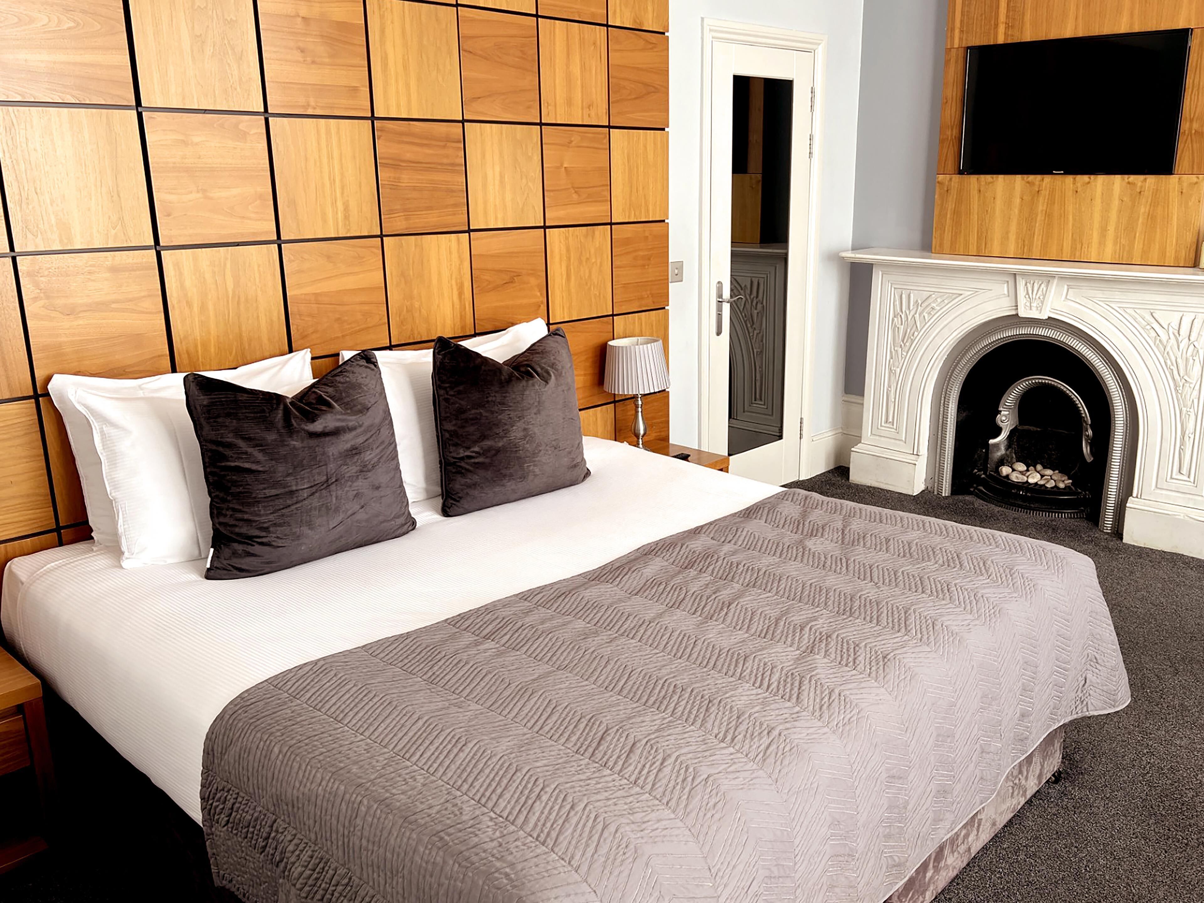 A hotel room with a large bed, a wooden headboard, a fireplace, and a television mounted above it.