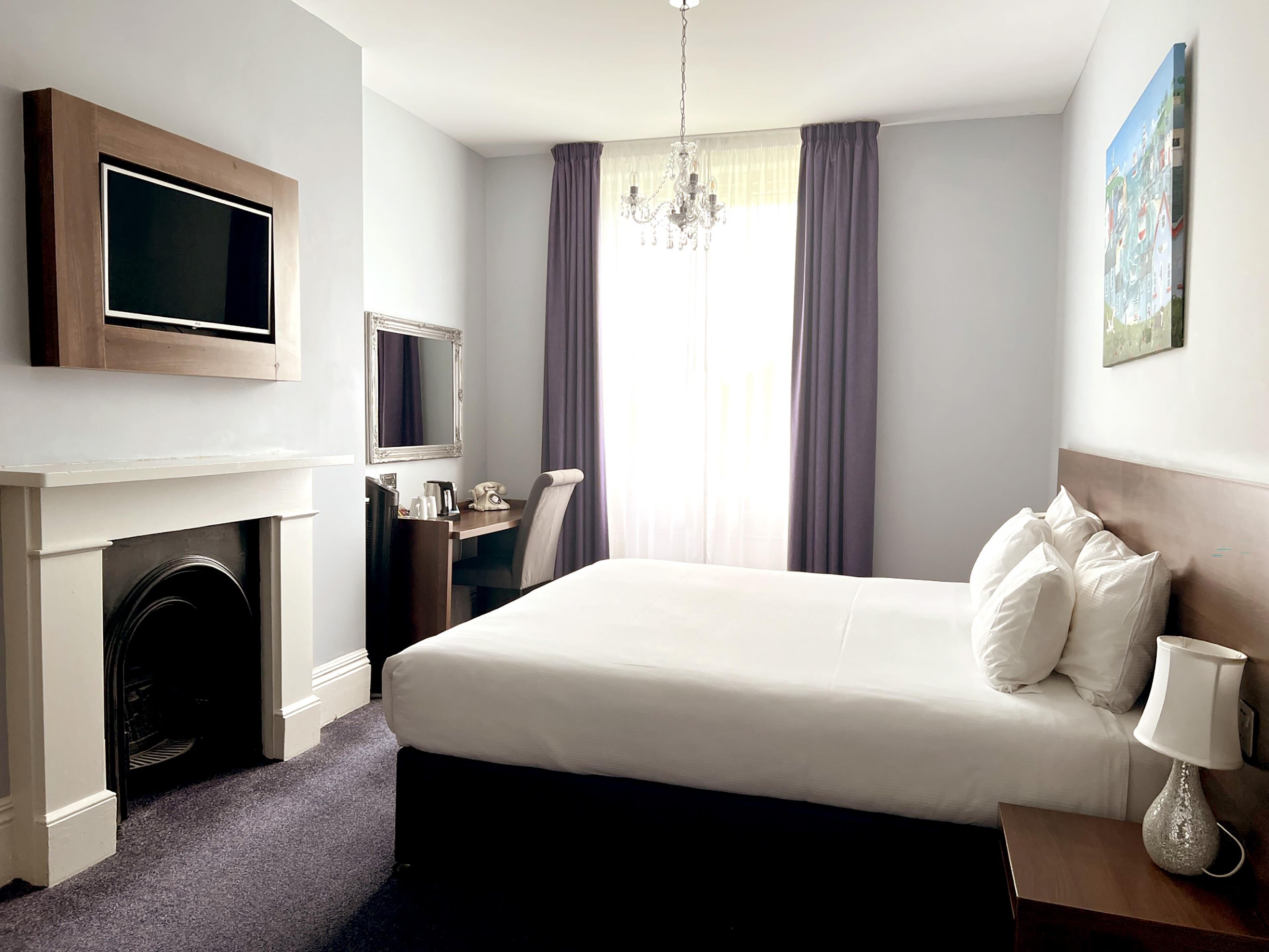 A hotel room with a bed, a desk, a television, a fireplace, and a chandelier.