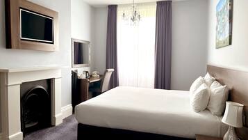 A hotel room with a bed, a desk, a television, a fireplace, and a chandelier.