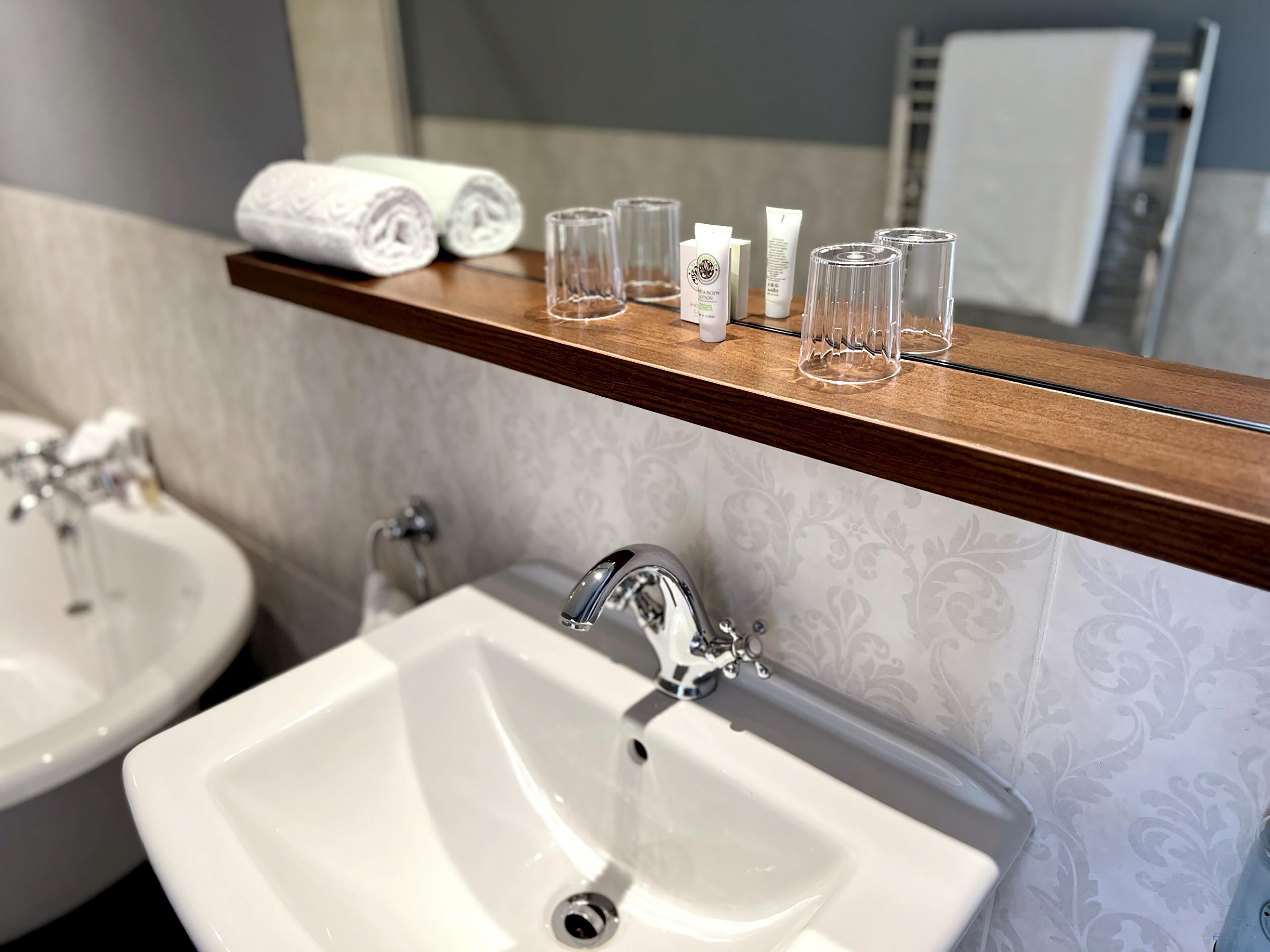Un baño con dos lavamanos, un espejo y un estante con artículos de tocador.