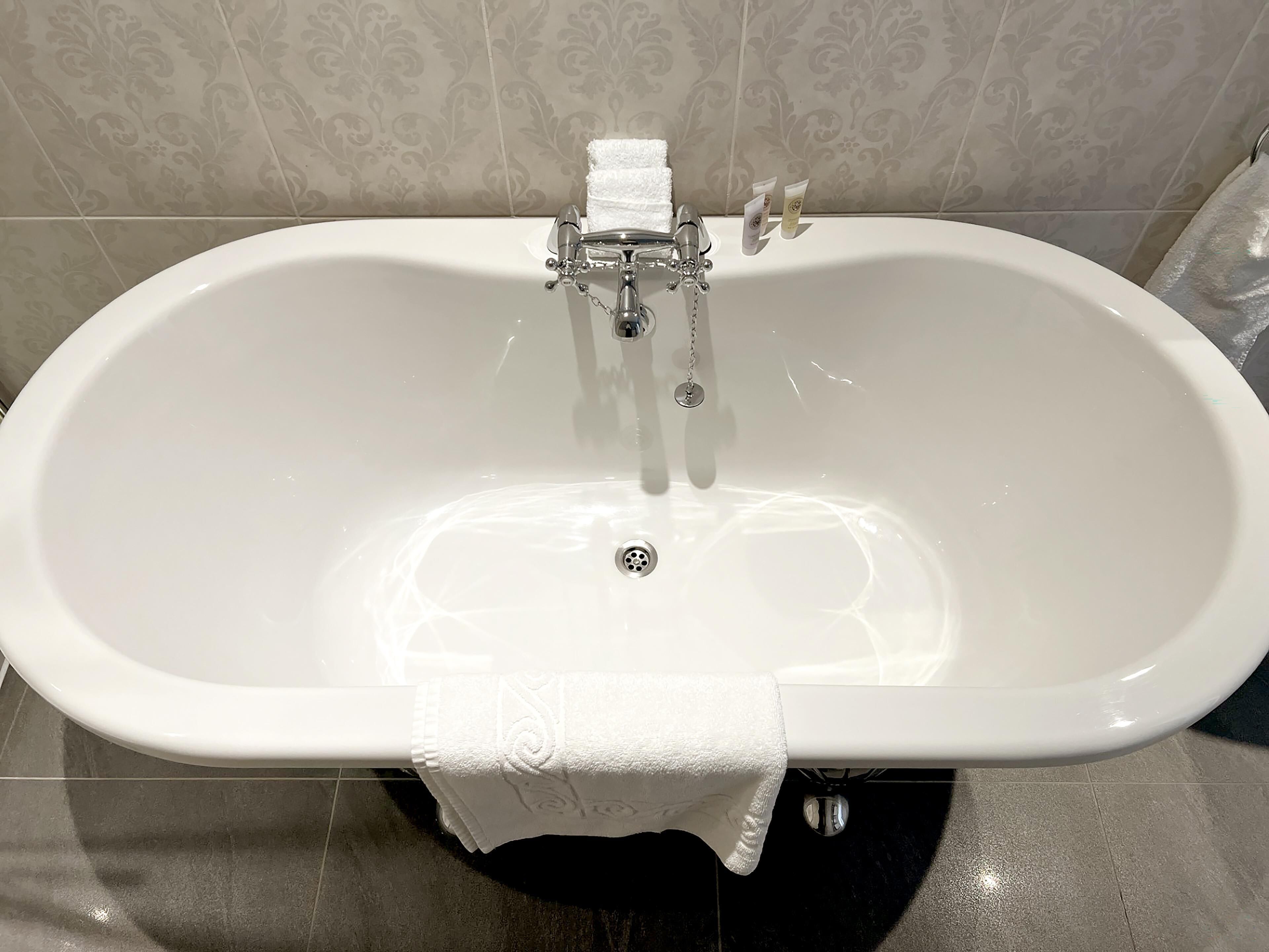 Una bañera blanca independiente con un solo grifo y desagüe, frente a una pared con diseño.