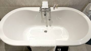 Una bañera blanca independiente con un solo grifo y desagüe, frente a una pared con diseño.