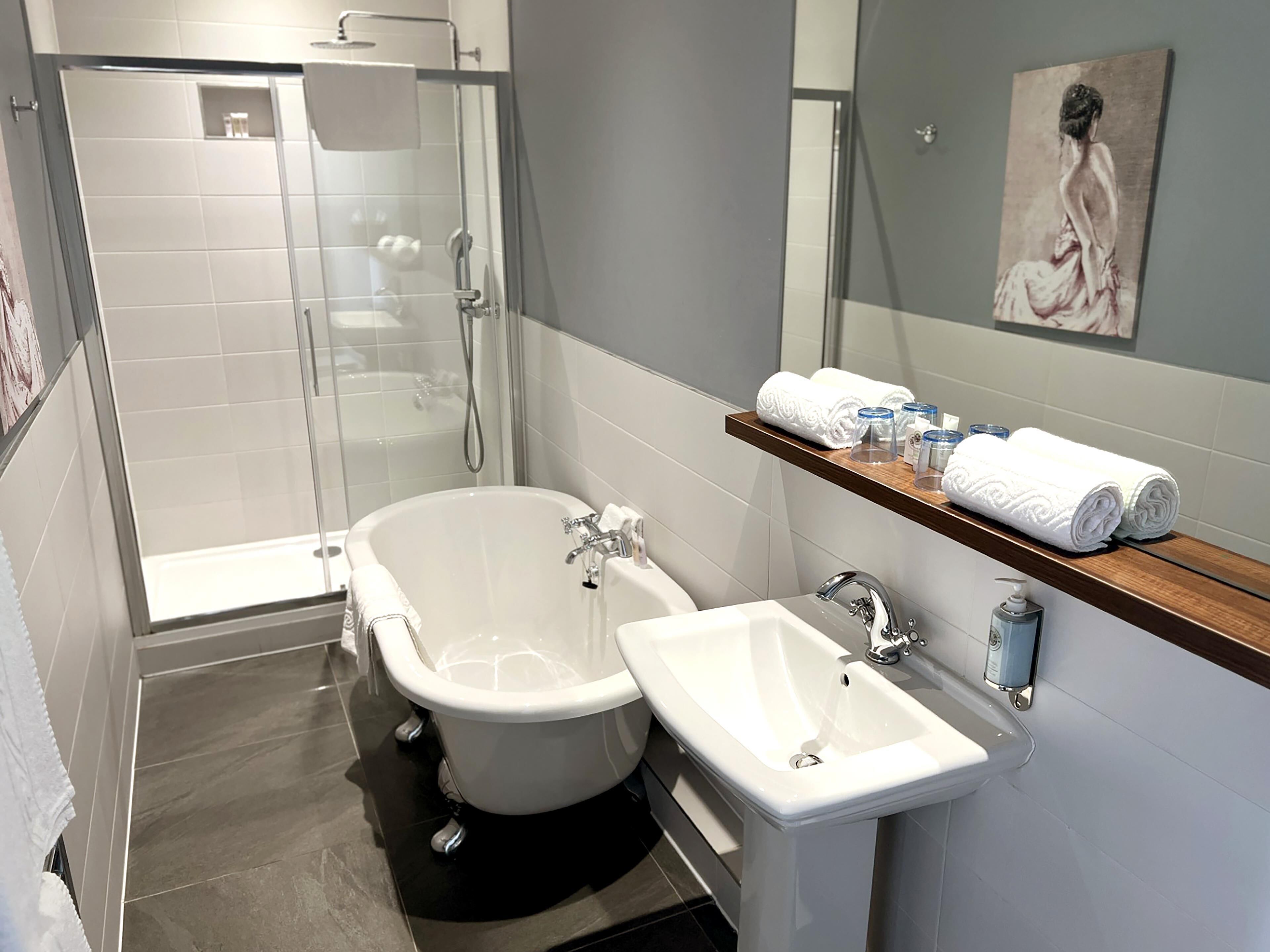Ein modernes Badezimmer mit einer gläsernen Duschkabine, einer freistehenden Badewanne und einem Waschbecken mit einem Holzboden darüber, auf dem Handtücher und Pflegeprodukte liegen.