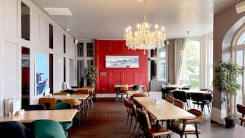 A restaurant with wooden tables and chairs, a red accent wall, and a chandelier.
