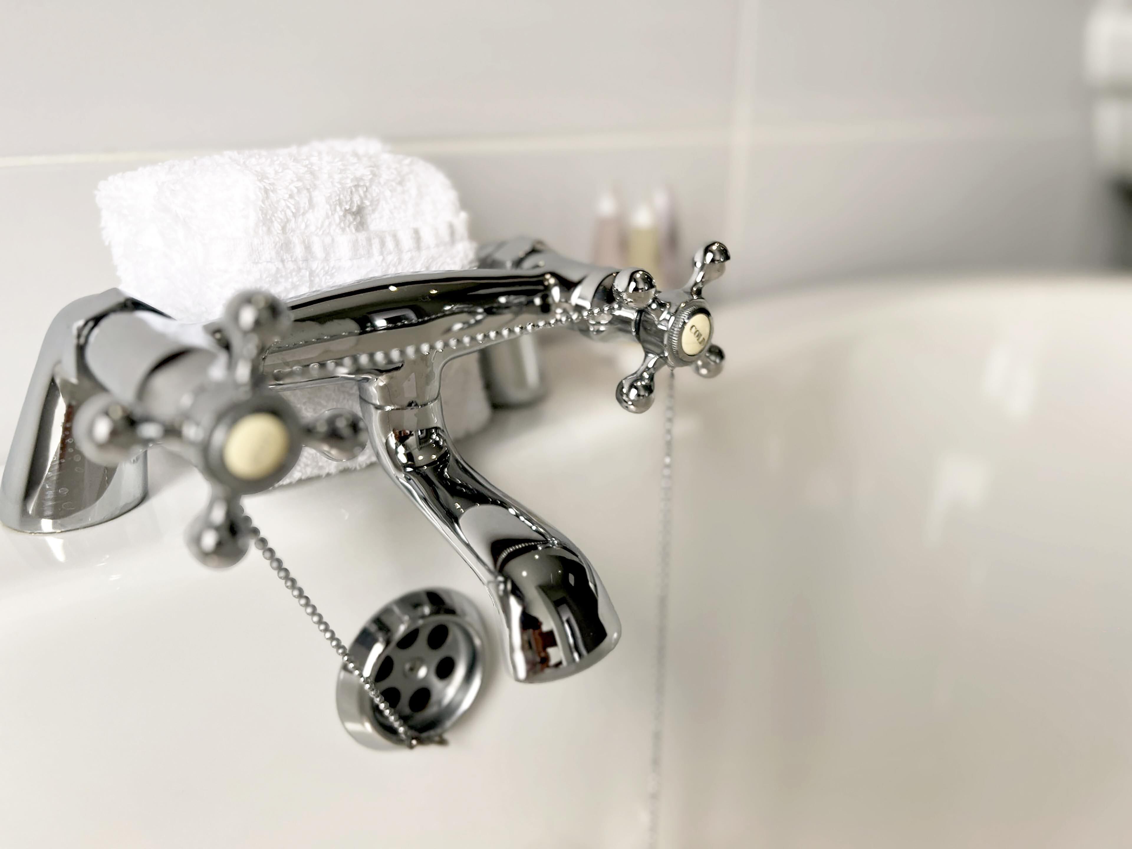 A bathroom with a chrome faucet, a soap dispenser, and a white towel hanging on the wall.