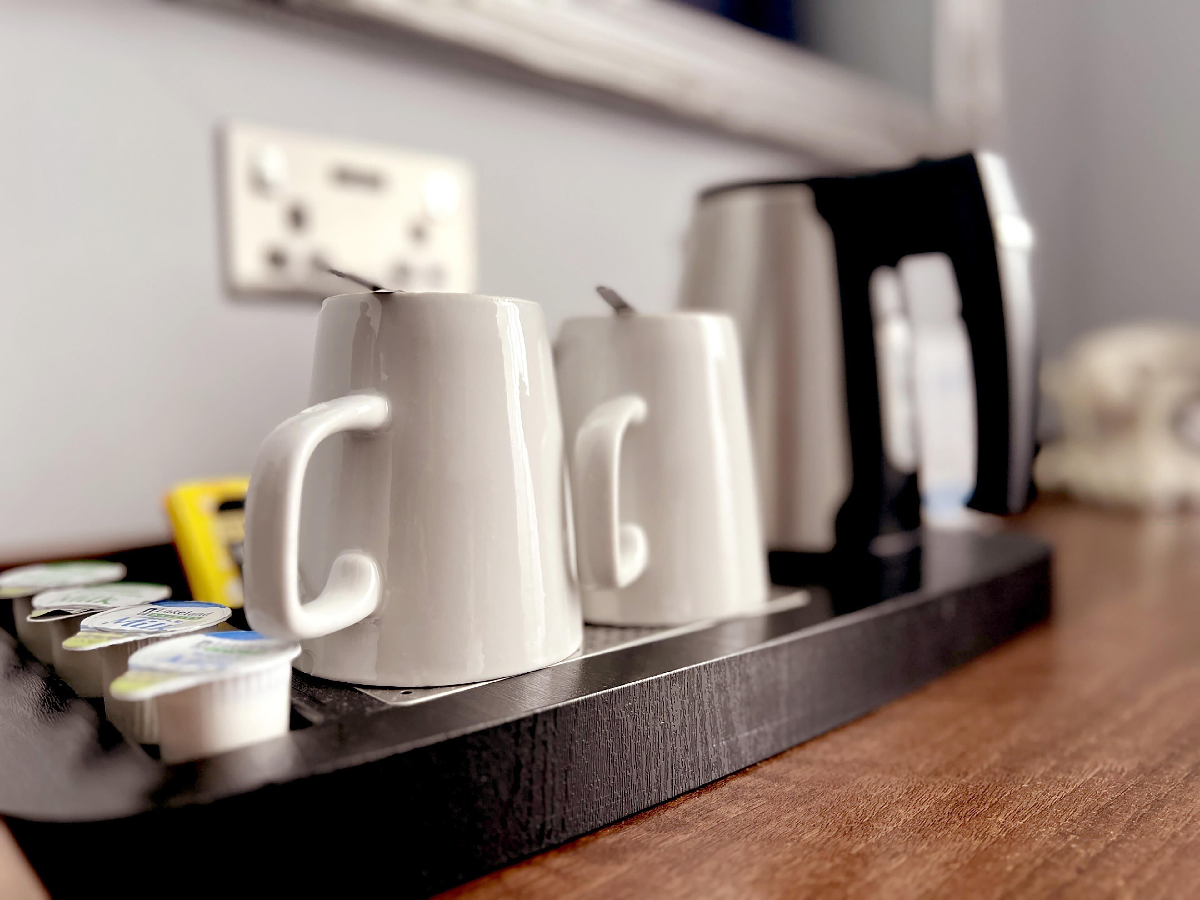 A tray with two white mugs, a black electric kettle, and a small container of yogurt on a wooden table.