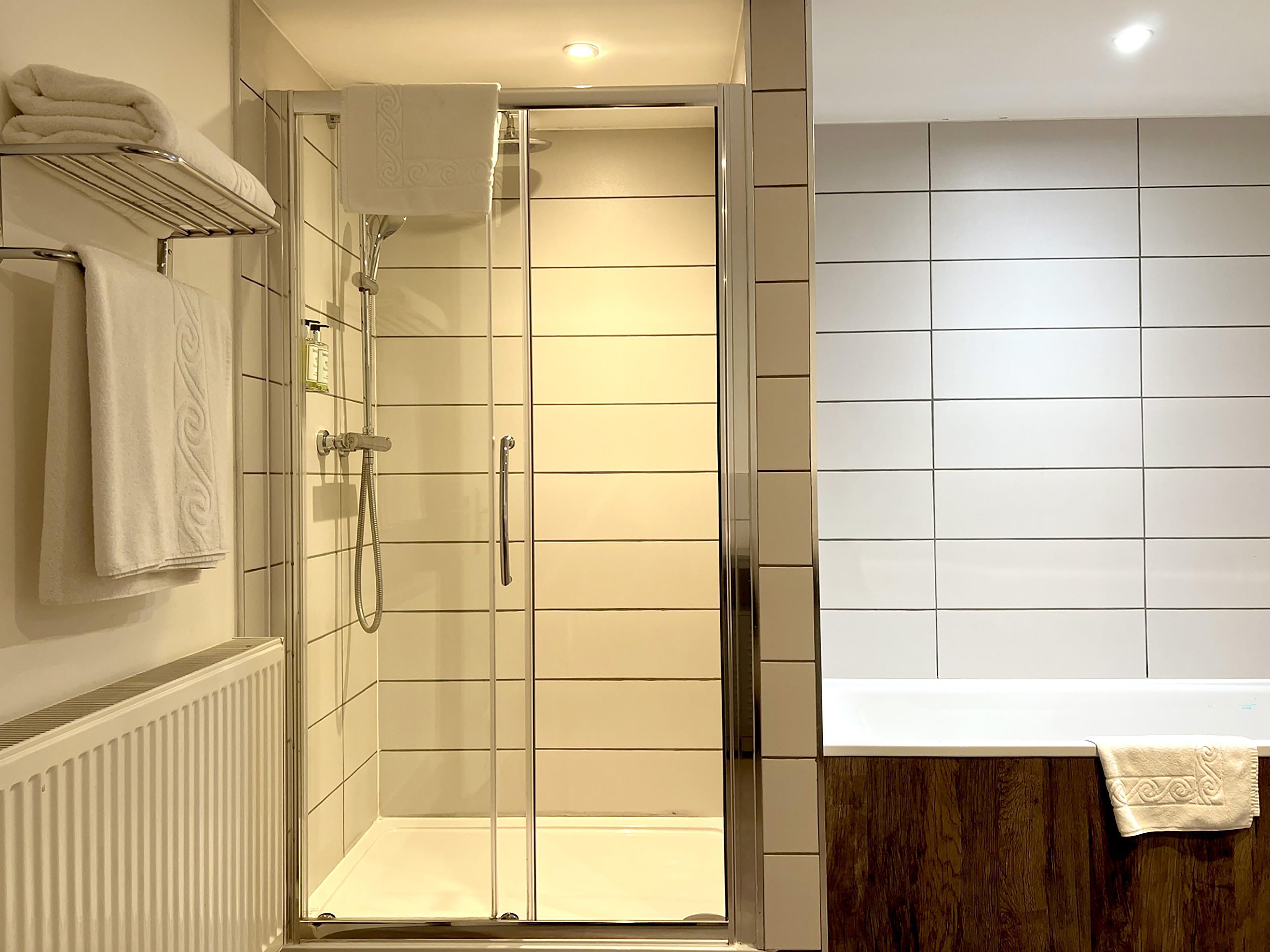 A modern bathroom with a glass-enclosed shower, a white tiled wall, and a wooden panel.