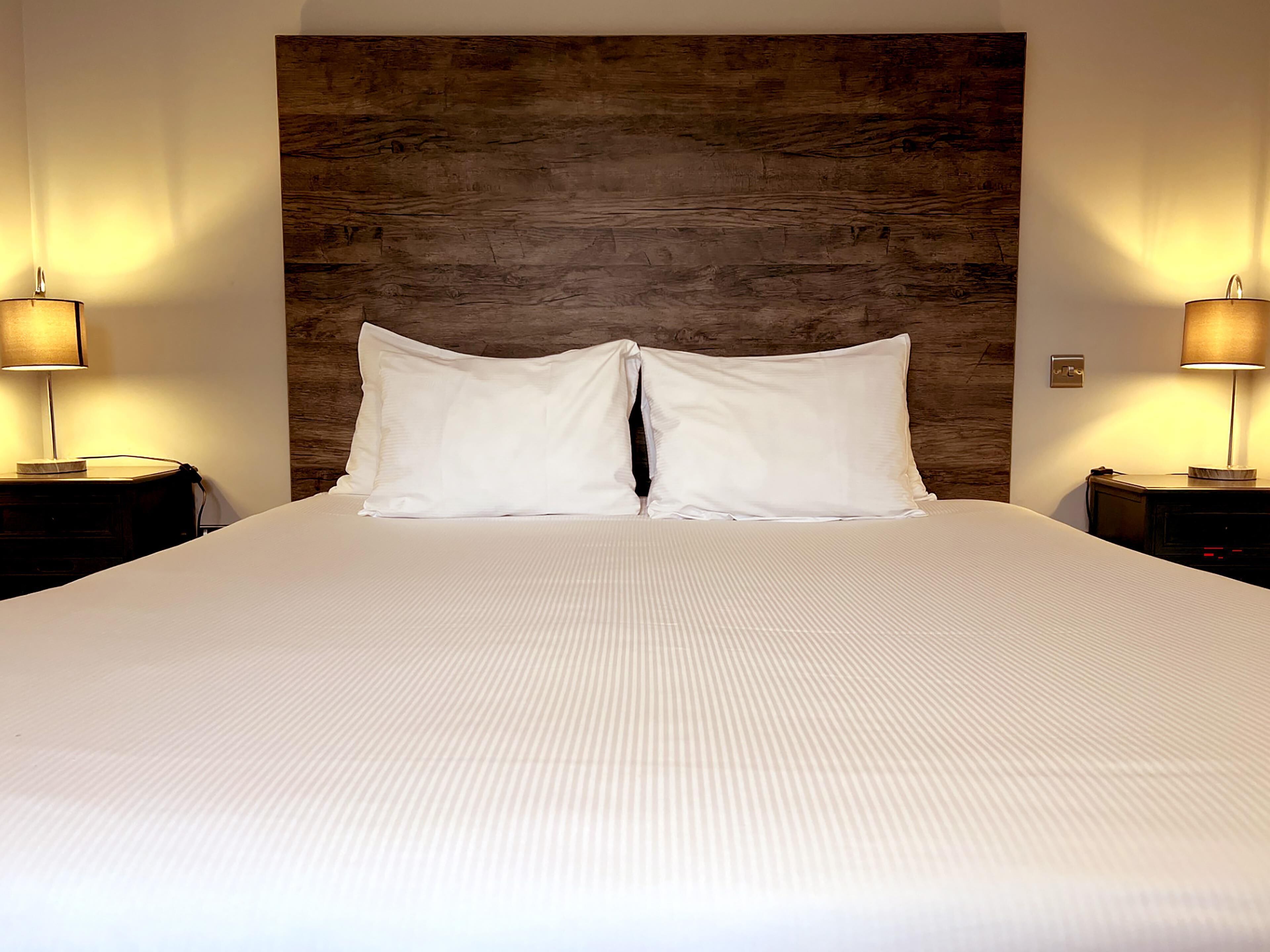 A neatly made bed with two pillows, a wooden headboard, and two bedside lamps on either side.