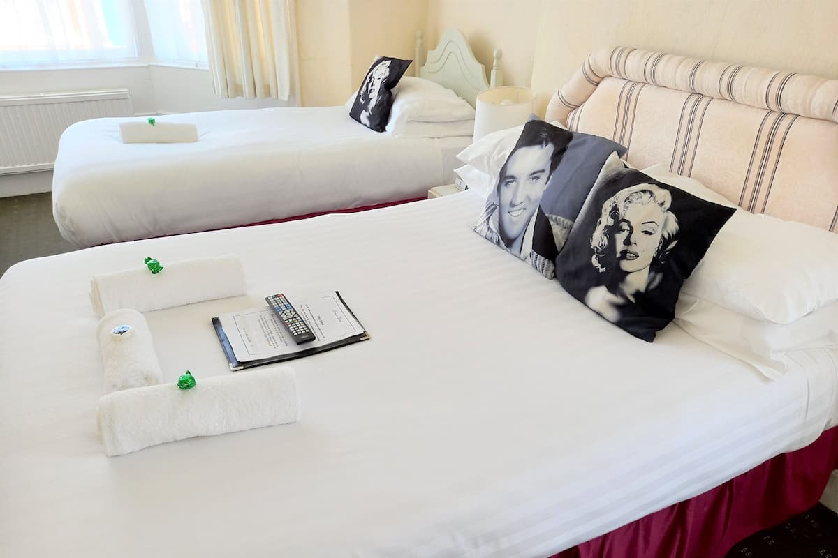 Two neatly made beds with white linens, pillows with a black and white design, and a remote control on the bed.