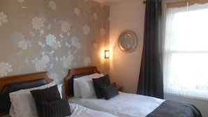 A hotel room with two beds, a wall-mounted mirror, and a window with curtains. - Ansteys Lea Guest House (Torquay)