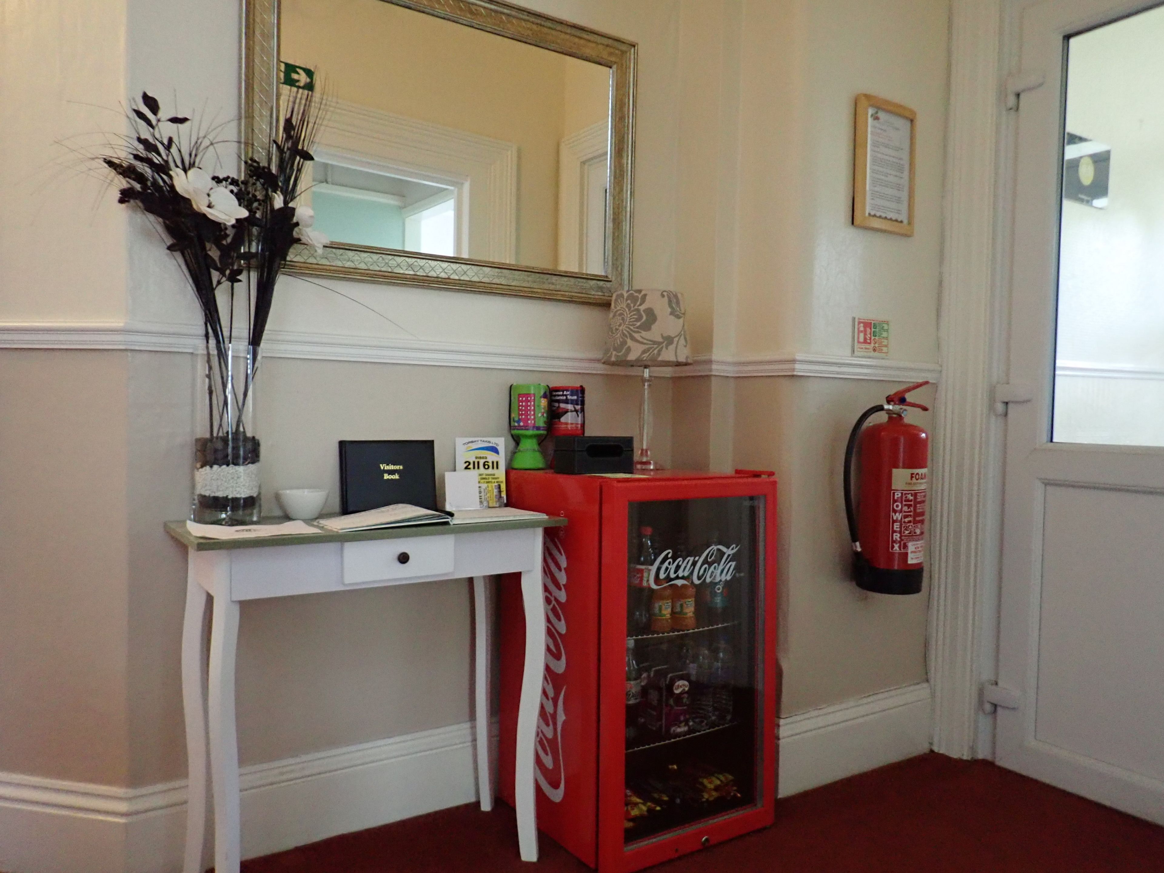 Un comptoir d’accueil avec un réfrigérateur Coca-Cola, un extincteur et un miroir au-dessus.