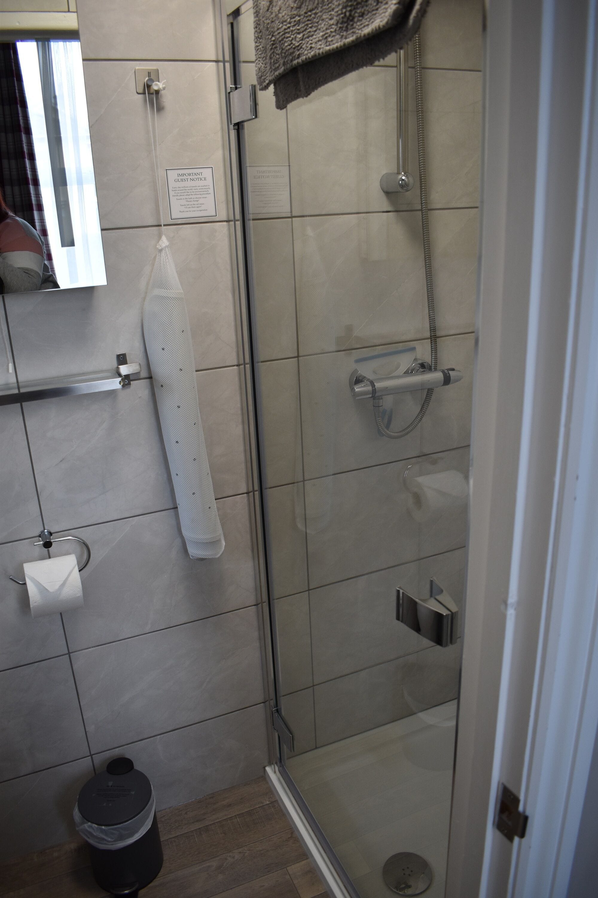A modern bathroom with a glass-enclosed shower, a towel rack, a trash bin, and a toilet paper holder.