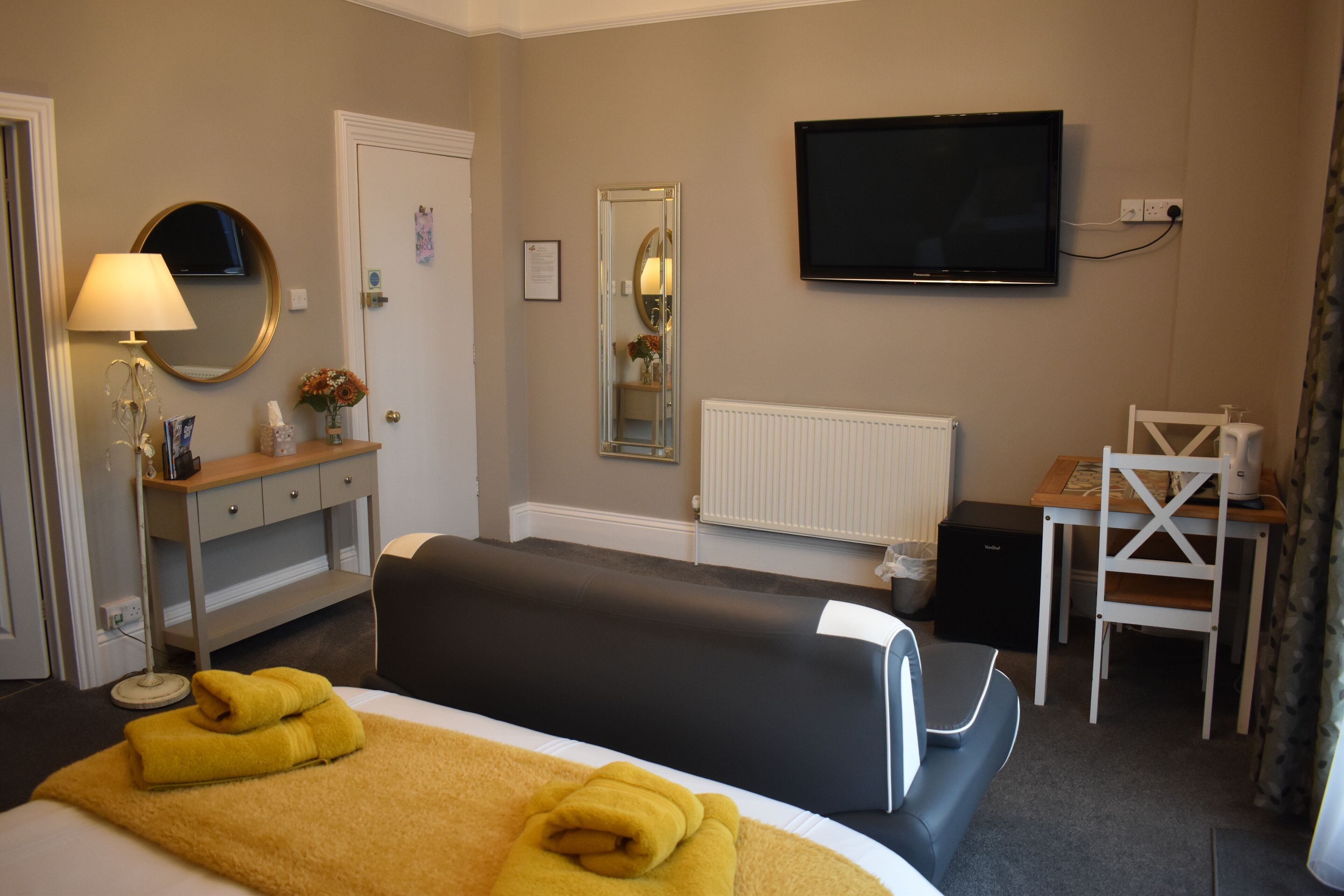 A hotel room with a bed, a desk, a chair, a TV, a mirror, and a lamp.