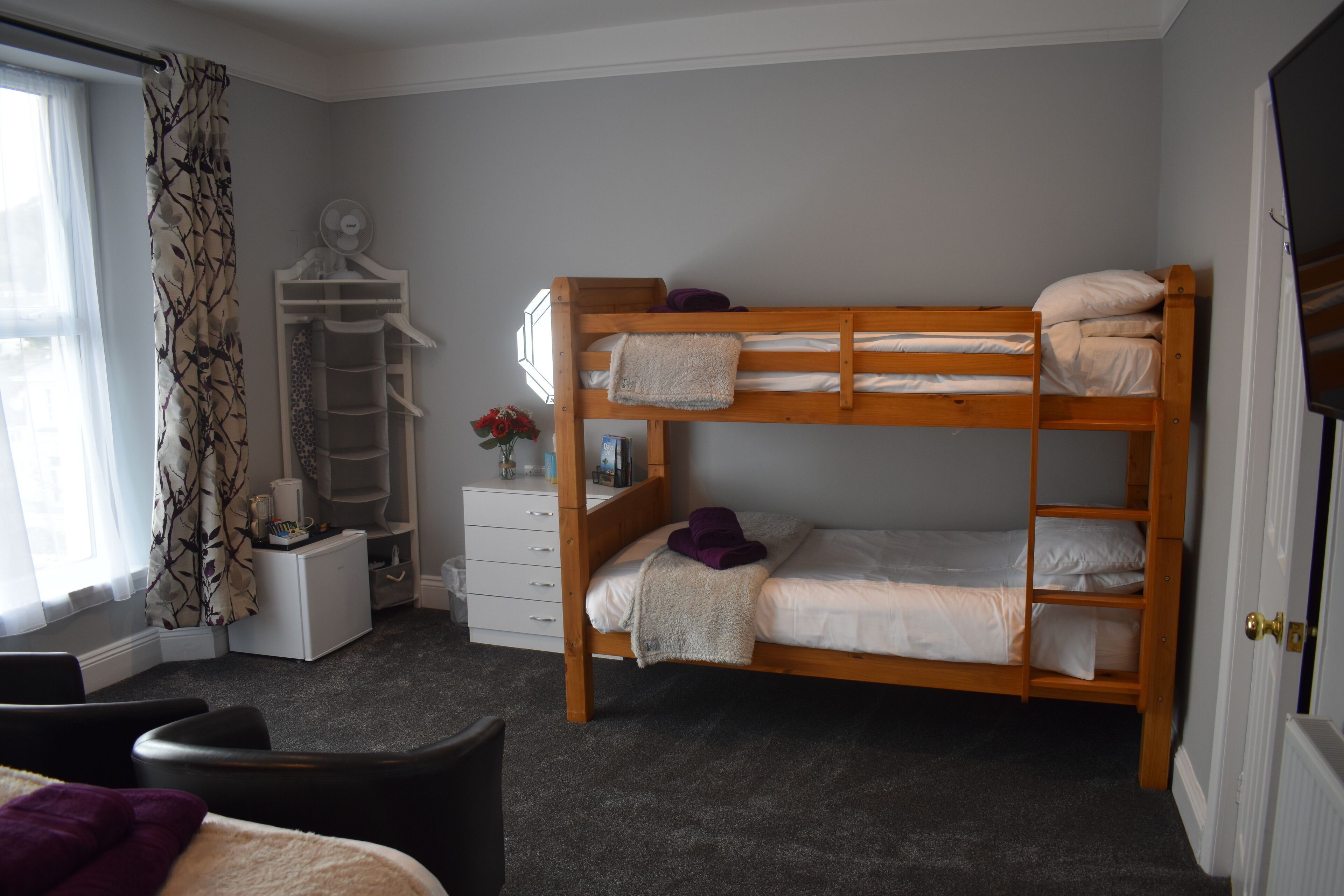 A bunk bed room with a desk, chair, and a window with curtains.