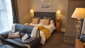 A hotel room with a bed, a sofa, two bedside tables with lamps, a framed picture on the wall, and a window with curtains. - Acorn Lodge (Torquay)