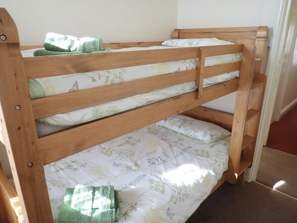 Una cama individual con ropa de cama estampada con motivos florales y una toalla verde.