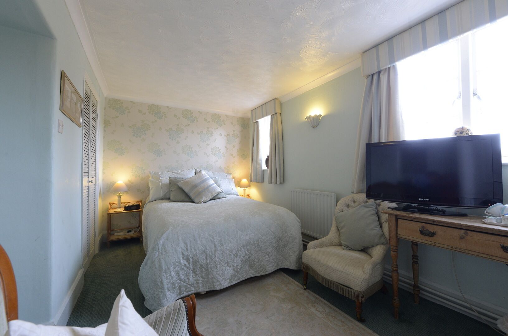 A bedroom with a bed, bedside lamps, a television, a chair, and a desk.