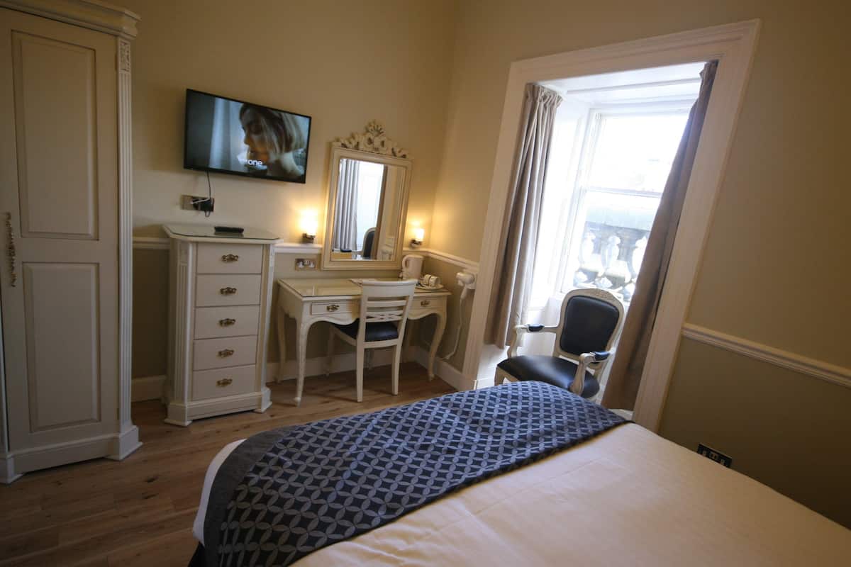A hotel room with a bed, a desk with a chair, a television, a mirror, and a wardrobe.