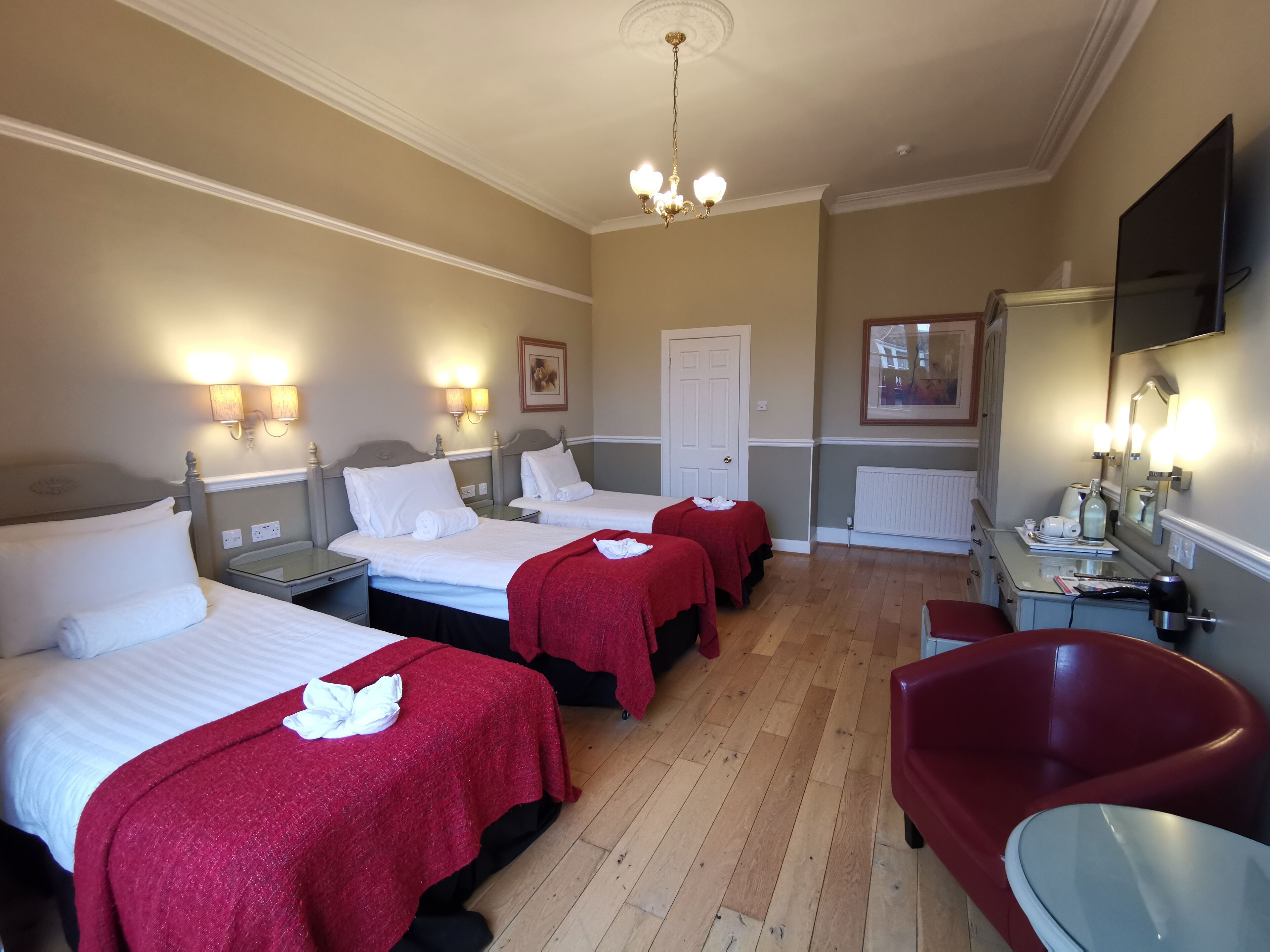 A hotel room with three beds, a red armchair, a small table, and a mirror.