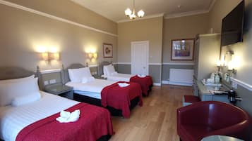 A hotel room with three beds, a red armchair, a small table, and a mirror.