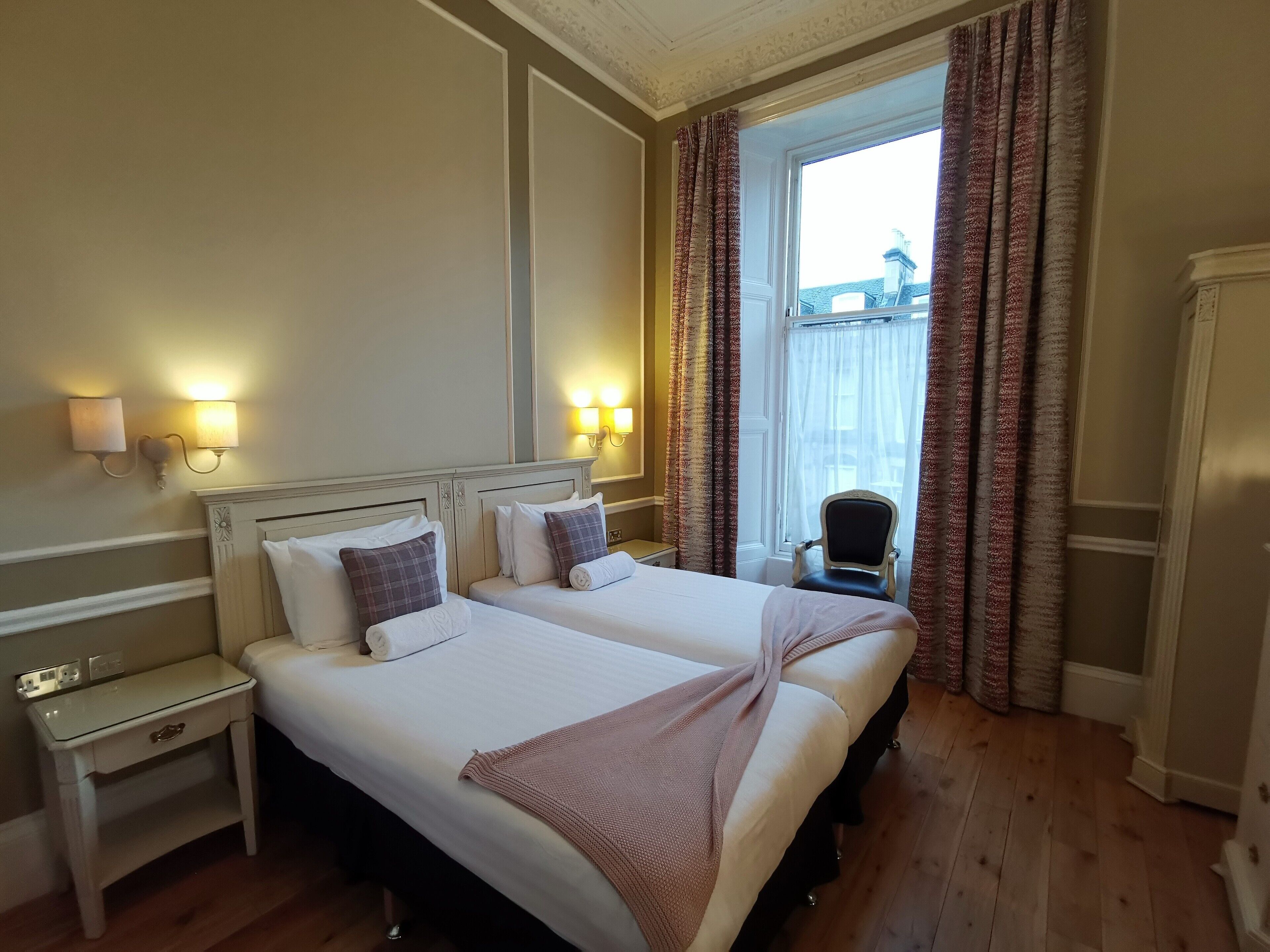 Habitación de hotel con dos camas, una mesita de noche, una silla y vista a un edificio a través de la ventana.