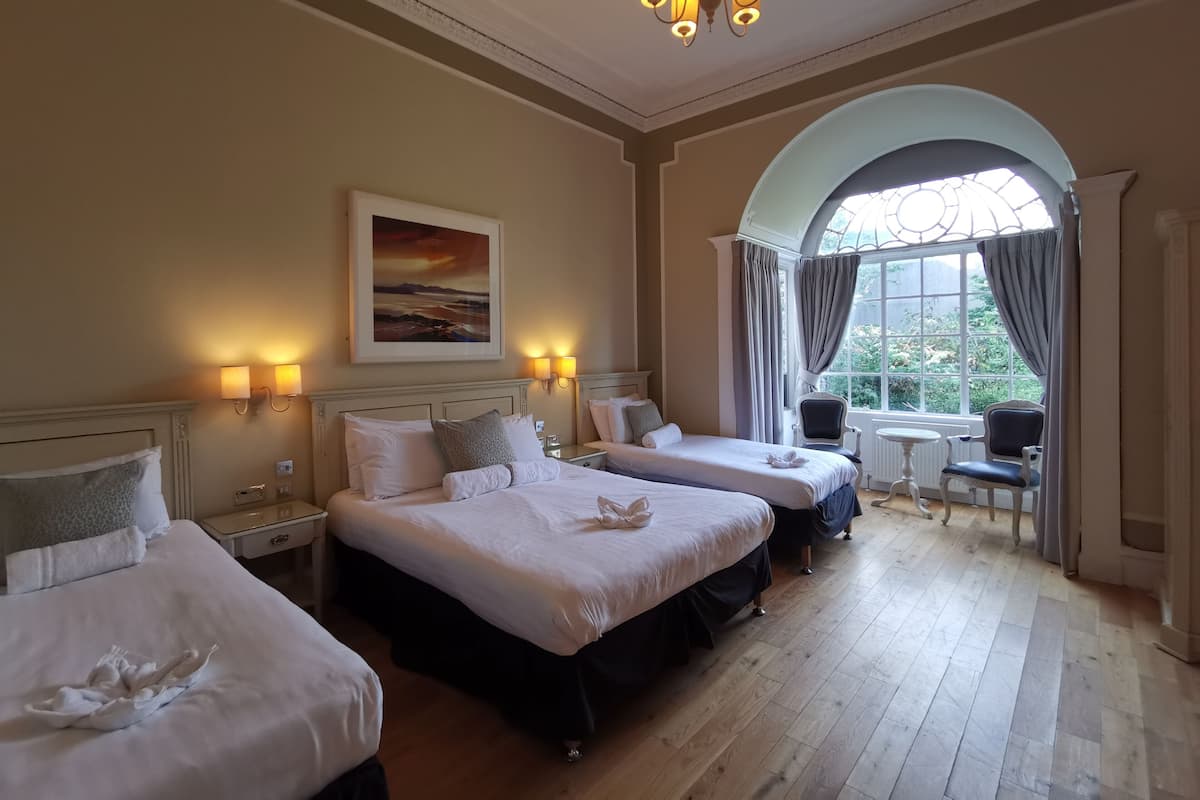 A hotel room with two beds, a painting on the wall, a chandelier, and a view through a window.