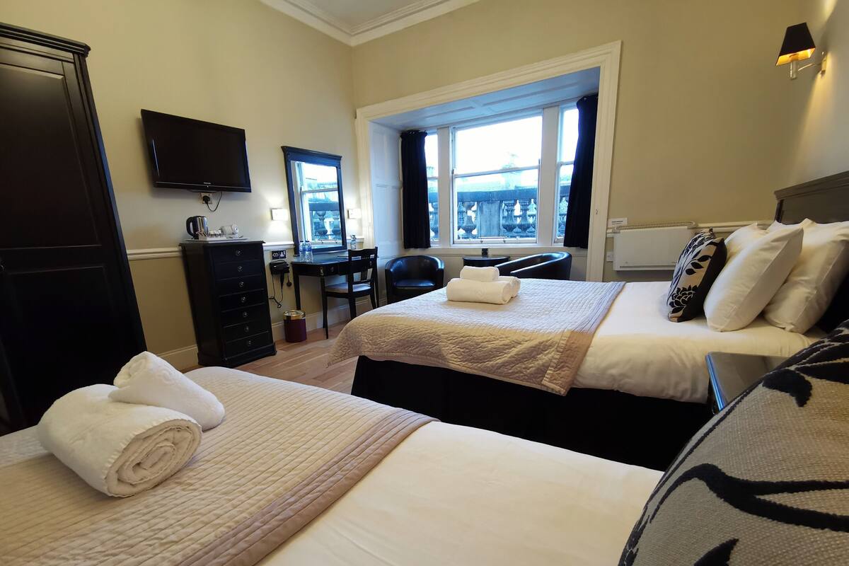 A hotel room with two beds, a desk, a chair, a television, and a window with a view.