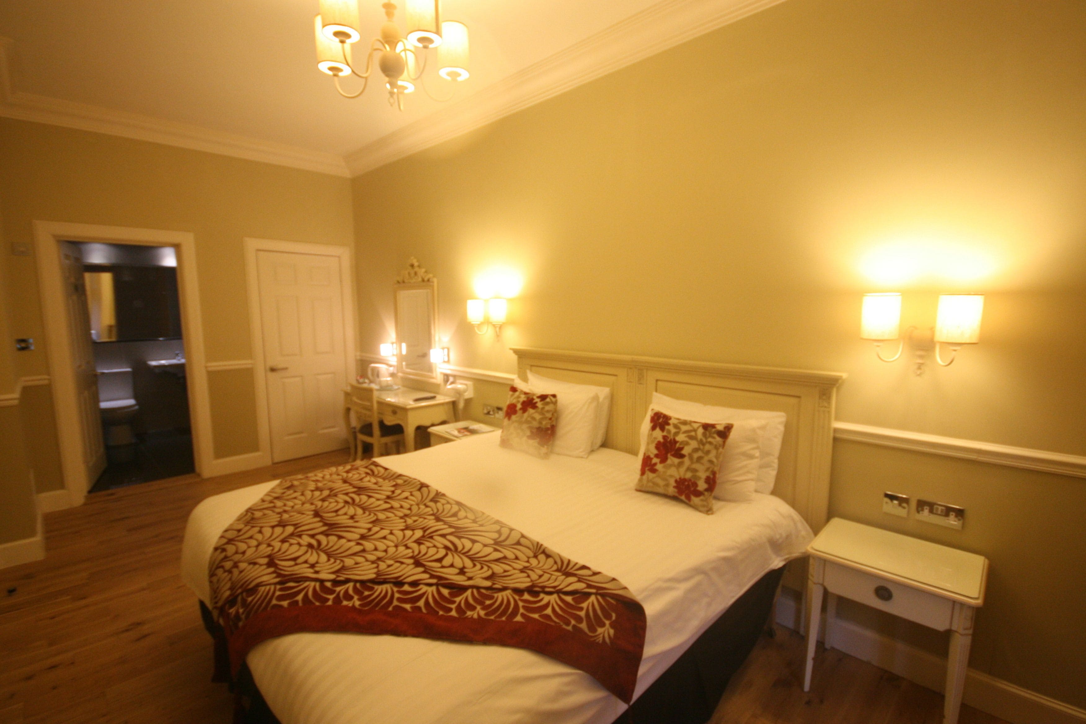 Una habitación de hotel con una cama grande, mesitas de noche, un escritorio y un espejo.