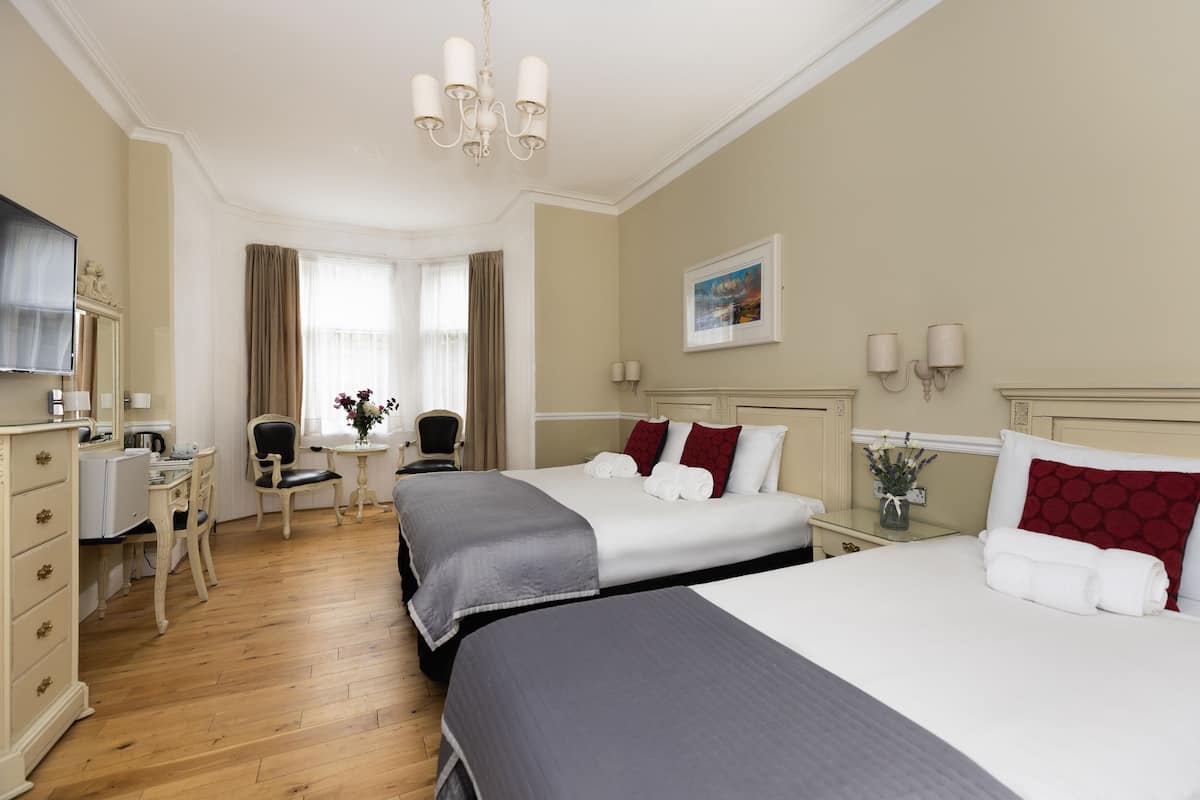 A hotel room with two beds, a desk, a chair, a TV, and a window with curtains.