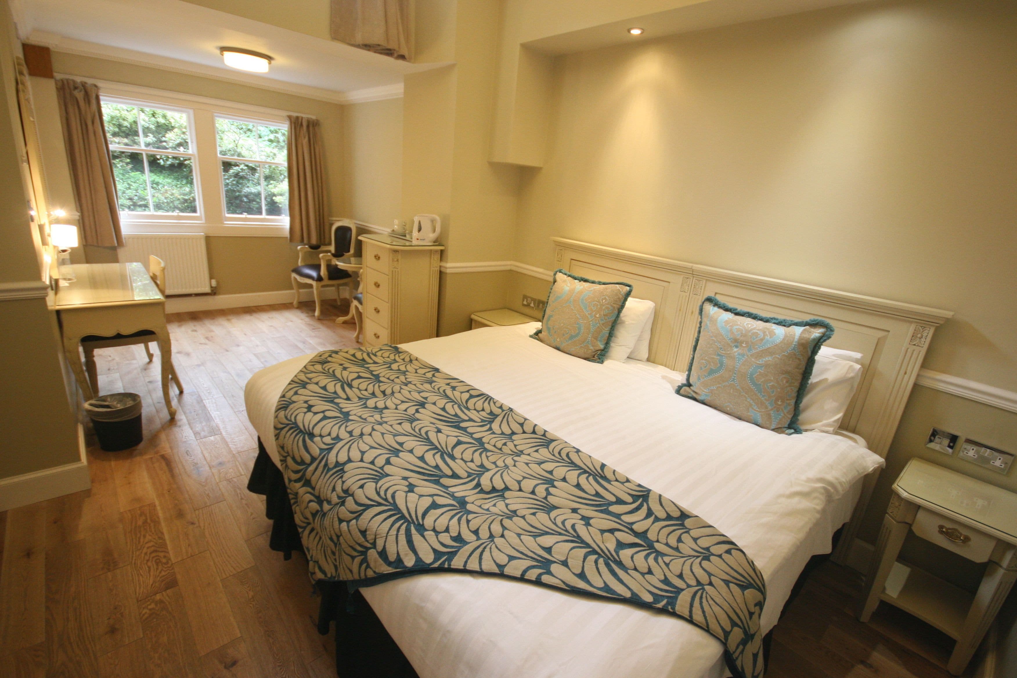 A hotel room with a large bed, a desk, a chair, and a small table.
