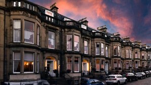 Una hilera de casas históricas adosadas, de arquitectura uniforme, con una calle empedrada y automóviles estacionados.