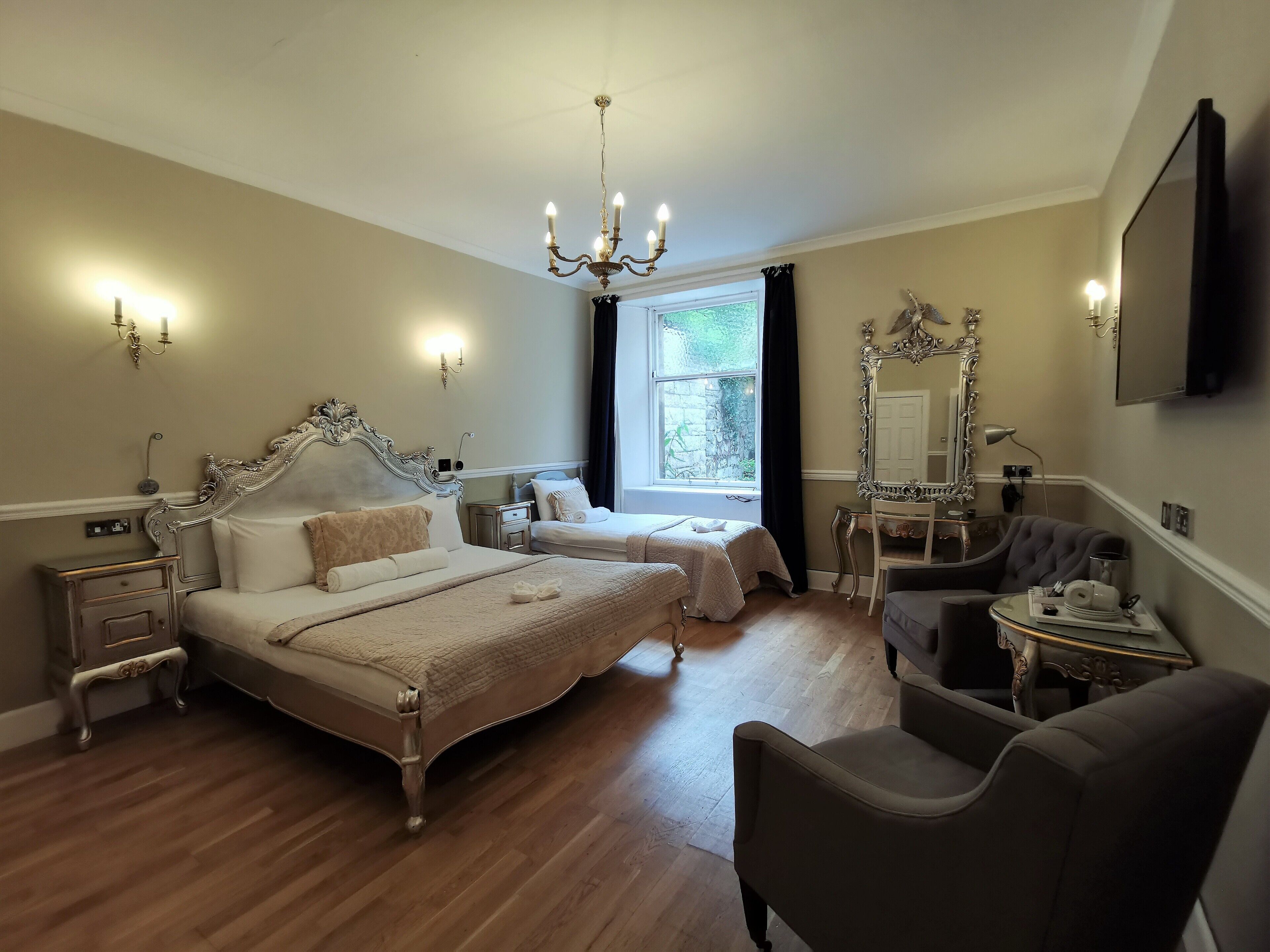 A spacious bedroom with a large bed, a smaller bed, a vanity with a mirror, and a chair.