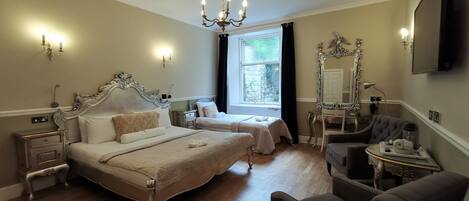 A spacious bedroom with a large bed, a smaller bed, a vanity with a mirror, and a chair.