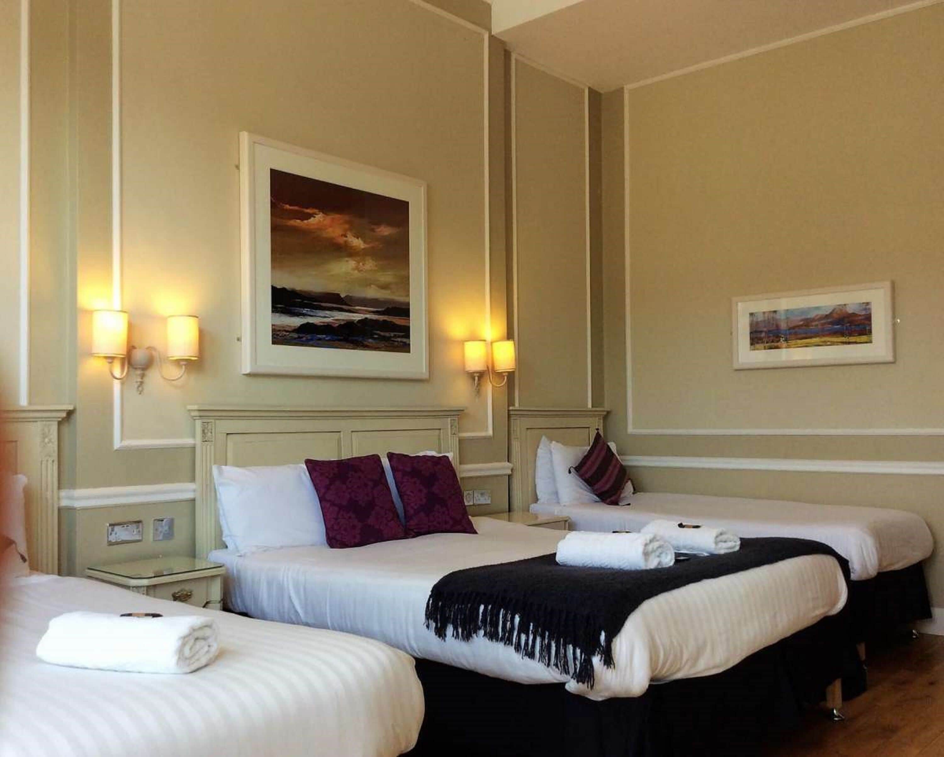 A hotel room with two beds, a painting on the wall, and two wall-mounted lamps.