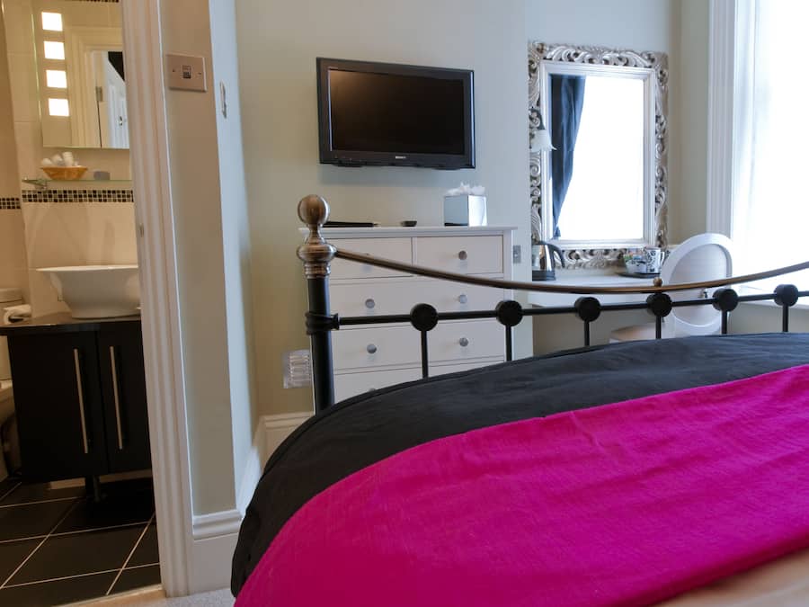 A bedroom with a bed, a dresser, a television, and a bathroom visible in the background.