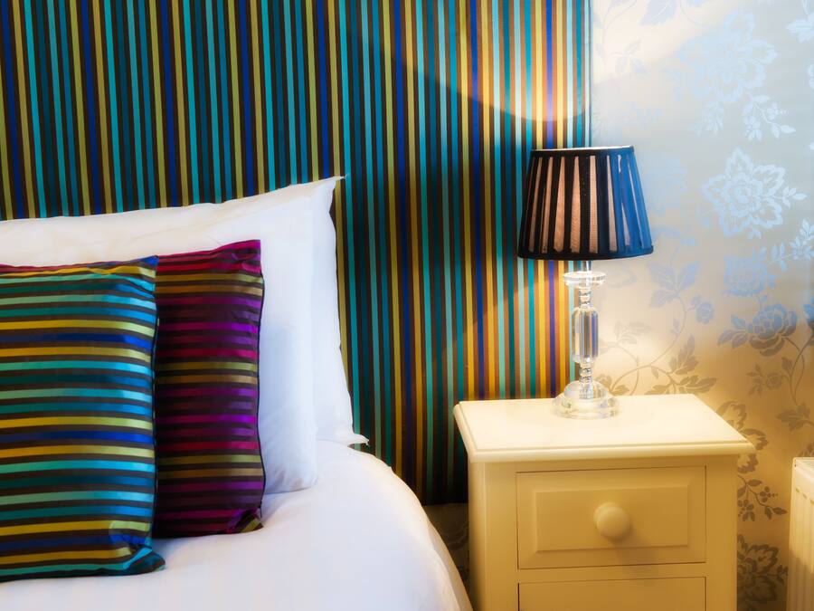 A bed with striped pillows, a bedside lamp, and a striped curtain in a hotel room.