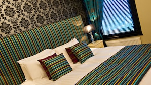 A neatly made bed with striped bedding, a bedside lamp, and a telephone on a nightstand. - The Grafton (Harrogate)